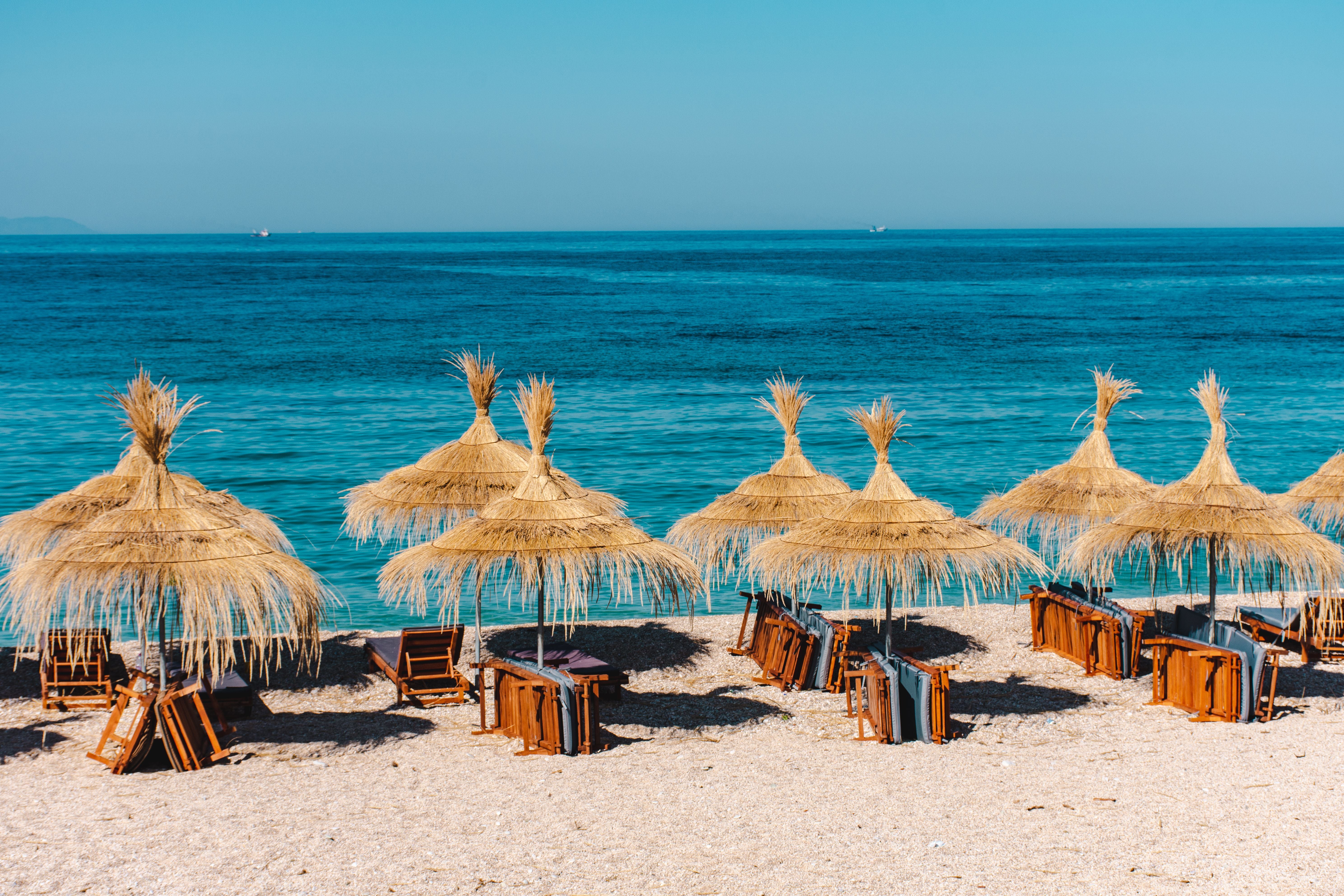 Strand in Himare, Albanien, mit Strohum­brel­las und Blick auf das blaue Meer.