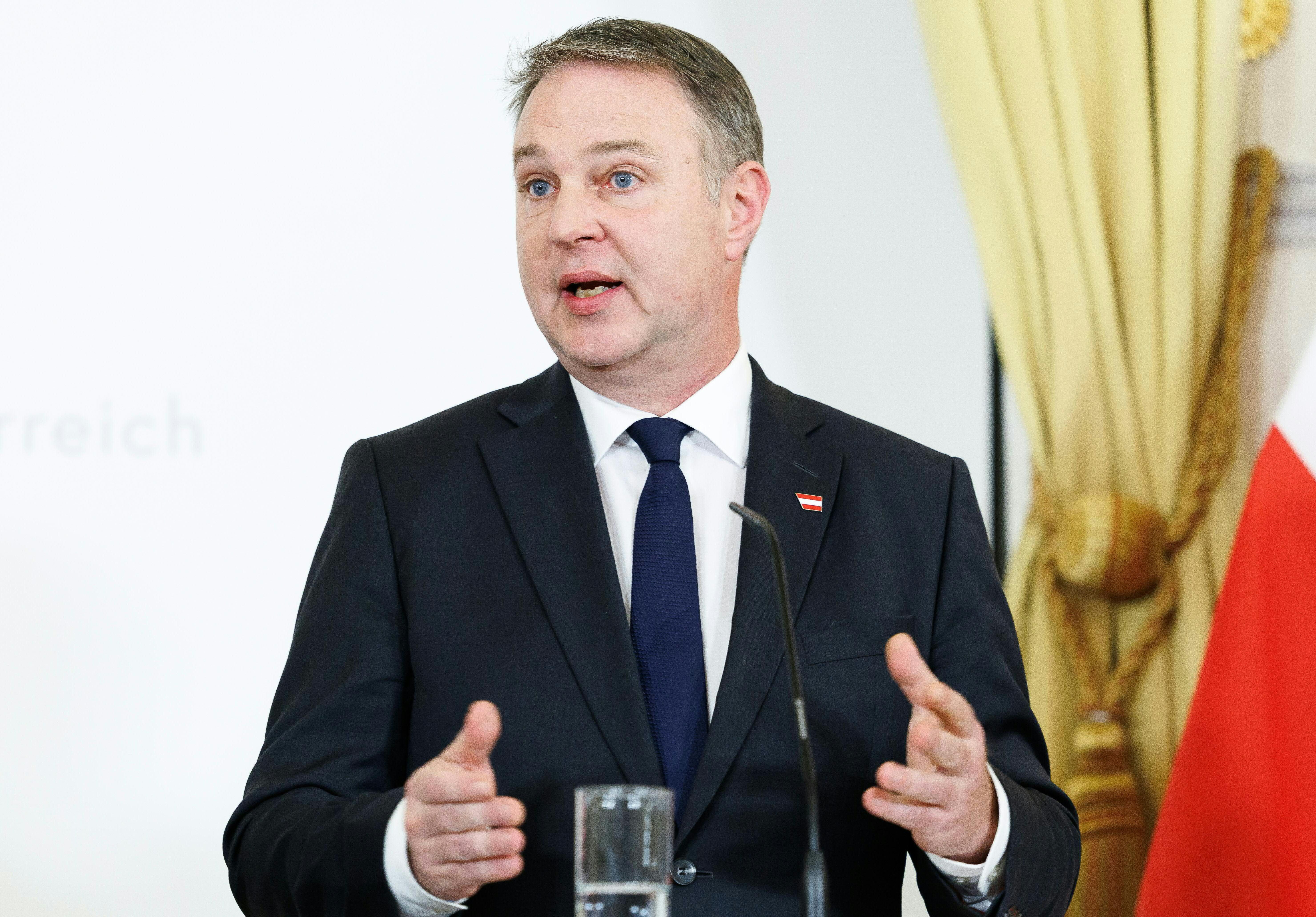 Andreas Babler spricht im Anzug bei einem Medienstatement vor Mikrofon und Glas Wasser.