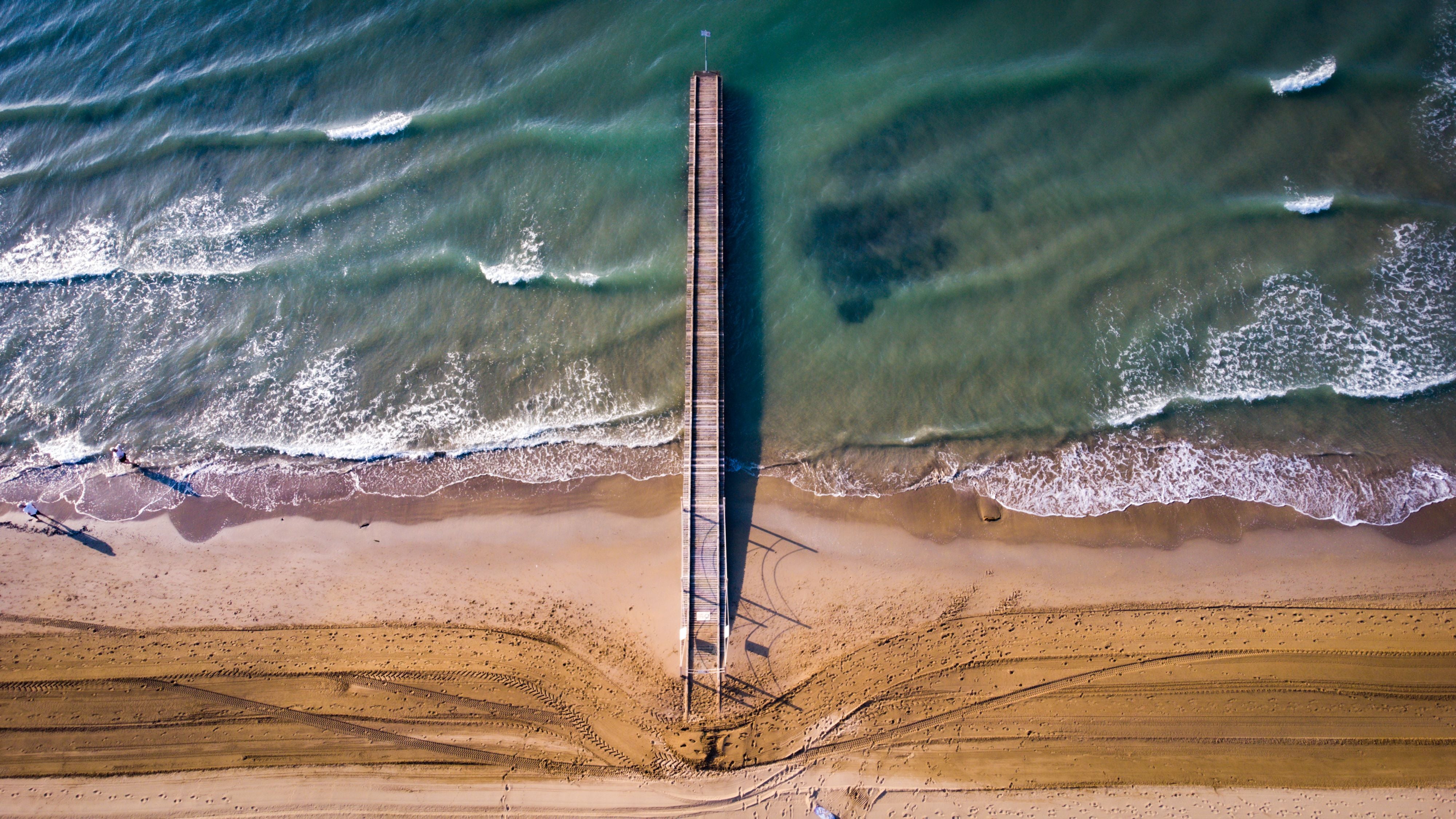 Luftaufnahme eines Stegs am Strand von Jesolo, Venedig, mit Wellen und Sand.