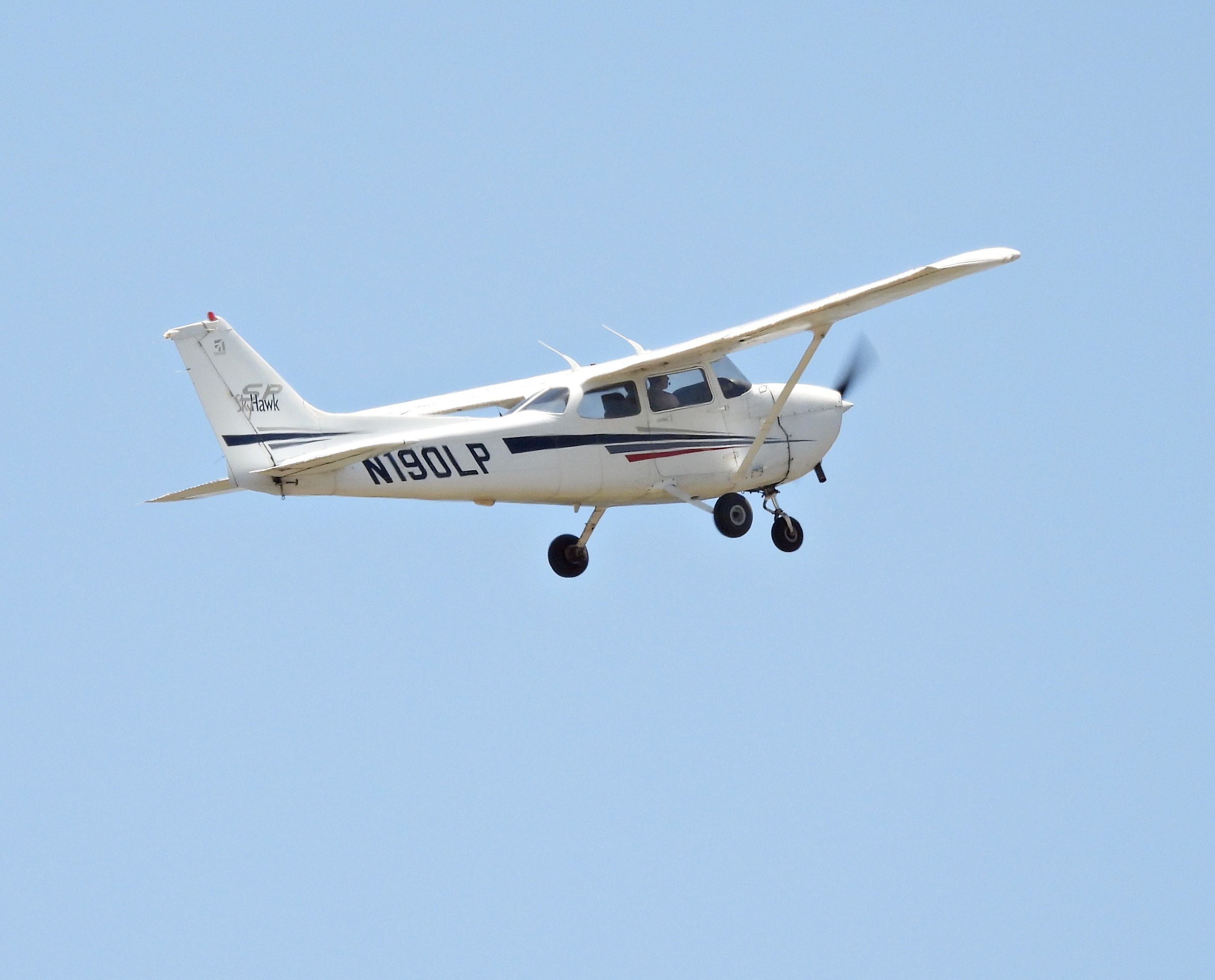 Kleine weiße Cessna 172S fliegt am klaren Himmel, Fahrwerk ausgefahren.