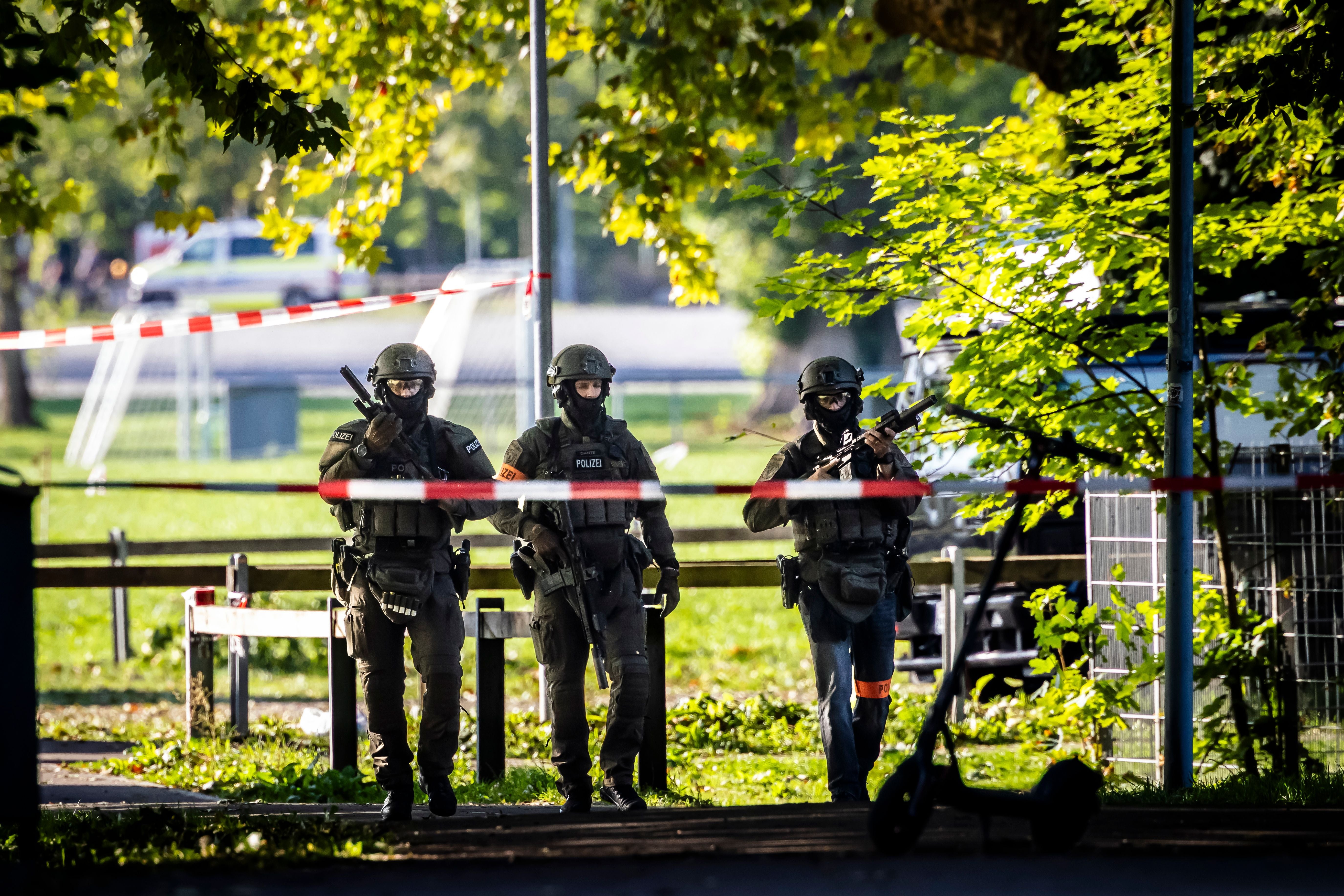 Drei schwer bewaffnete Polizisten patrouillieren abgesperrtes Gelände.