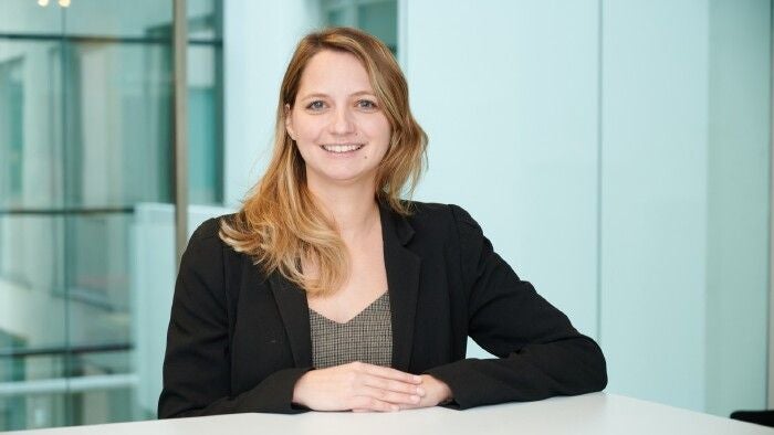 Junge Frau mit blondem Haar sitzt lächelnd an einem Tisch in modernem Büro.