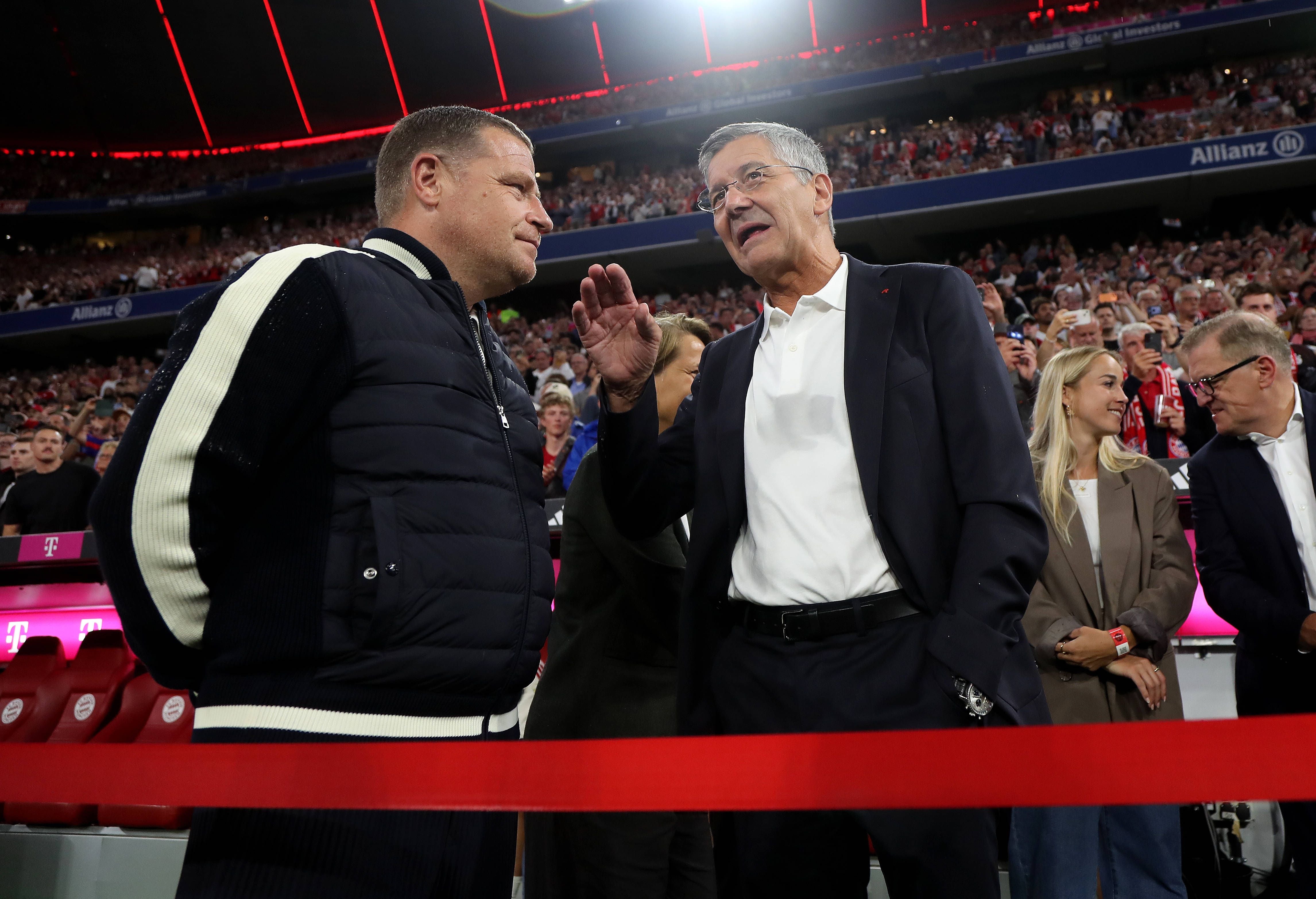 Zwei Männer unterhalten sich am Spielfeldrand in einem vollen Fußballstadion.