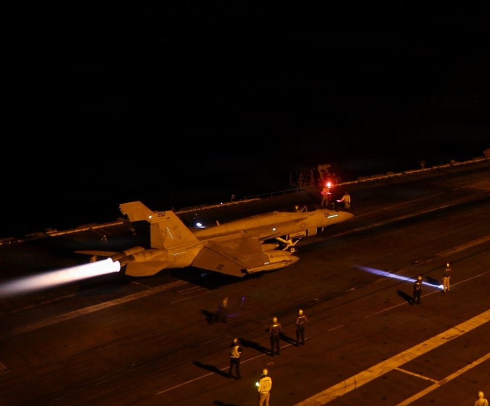 Ein US-Kampfjet startet nachts von einem Flugzeugträgerdeck.
