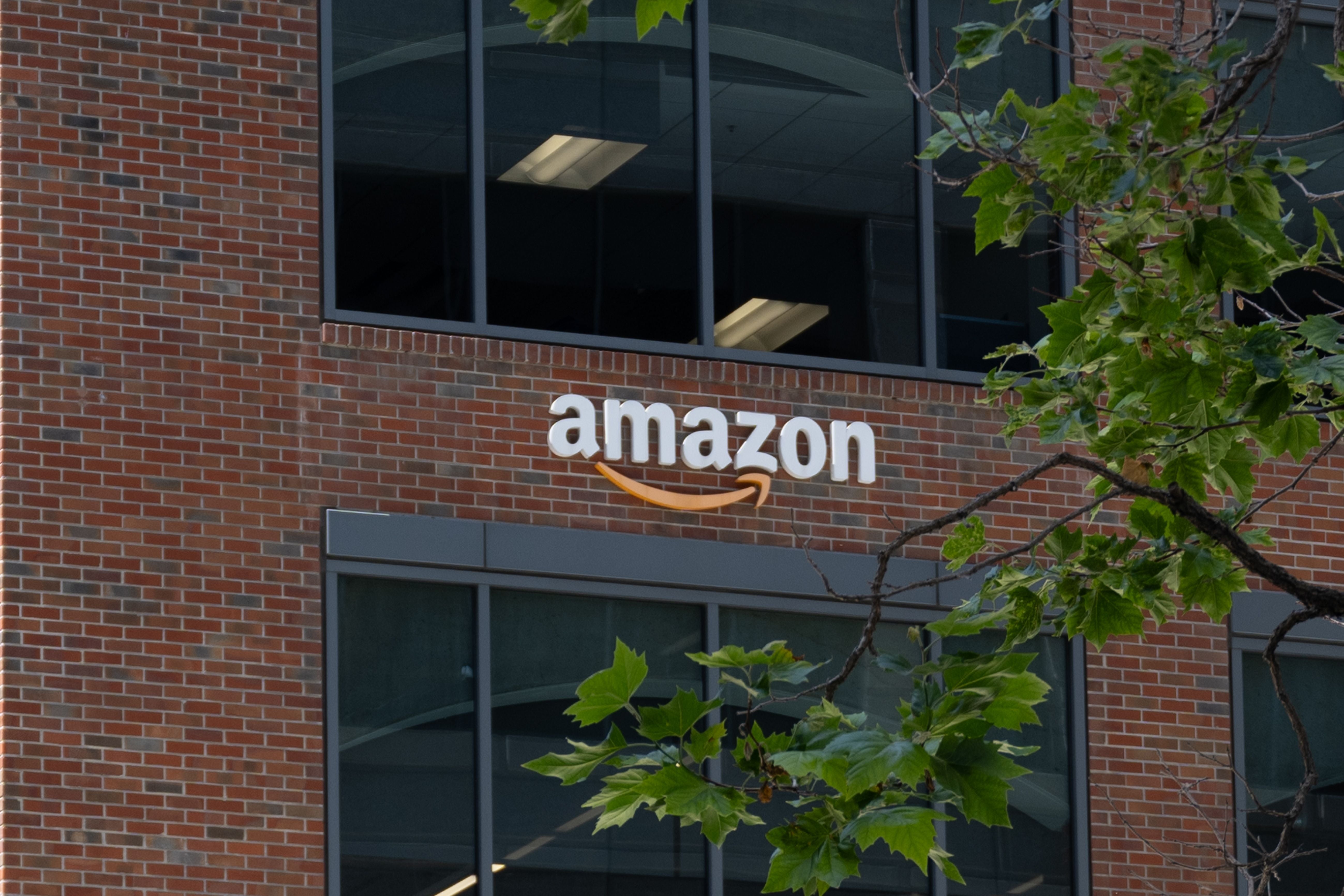 Amazon-Logo an einer Backsteinfassade eines Bürogebäudes mit Fenstern und grünen Blättern.