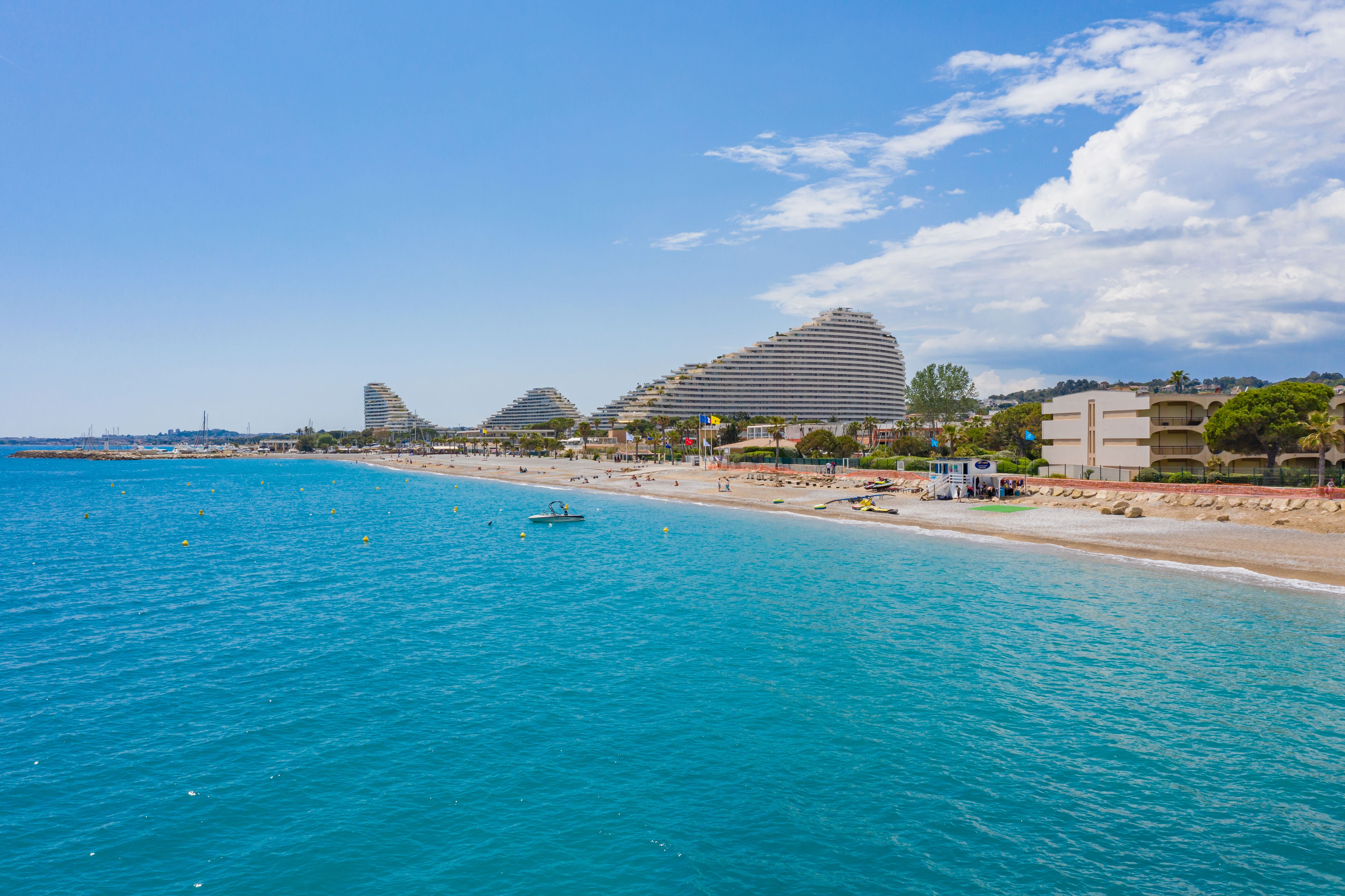 Strand an der französischen Riviera mit türkisblauem Meer und modernen Wohngebäuden im Hintergrund.