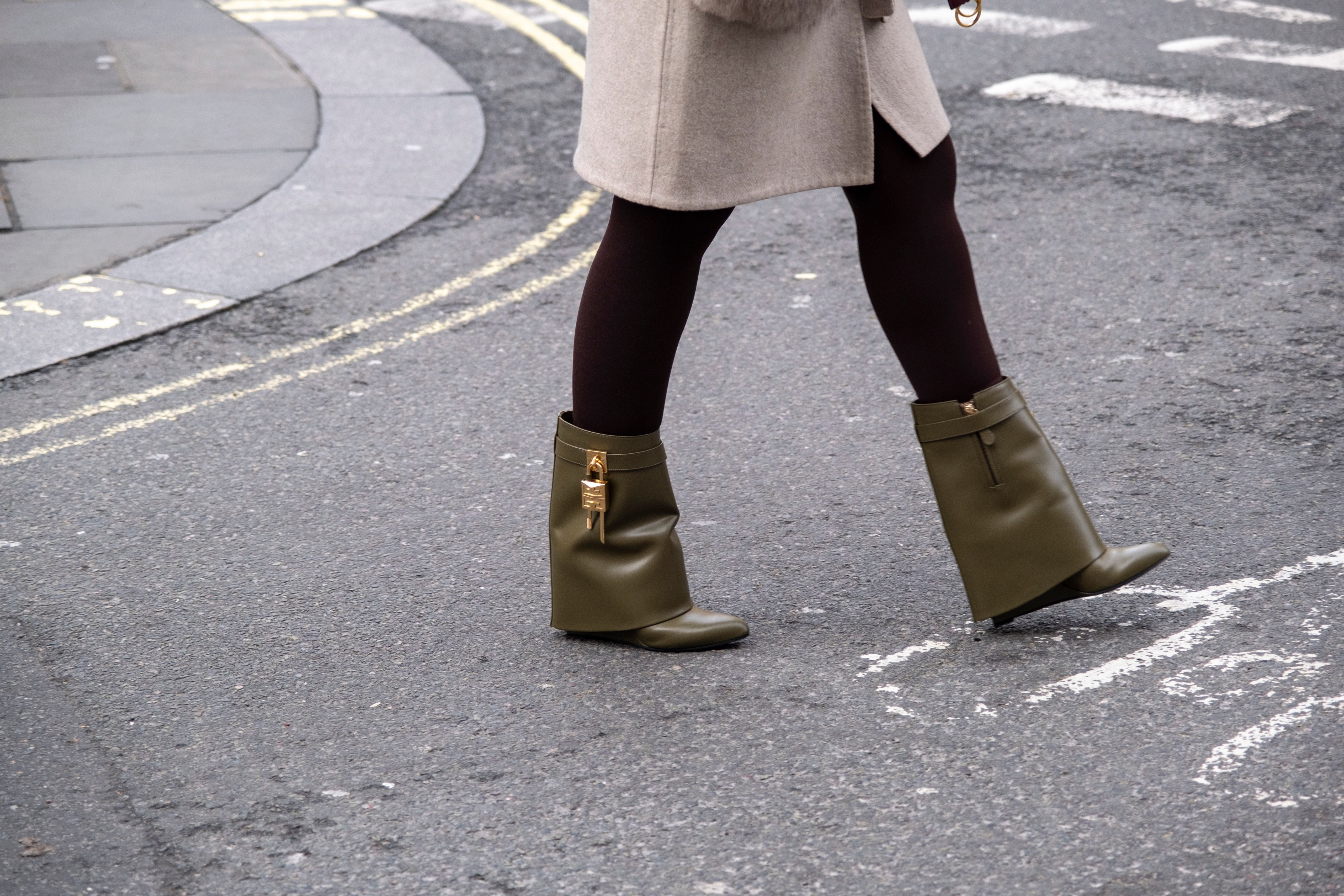 Frau mit khakifarbenen Stiefeletten mit goldenen Details auf einer Straße.