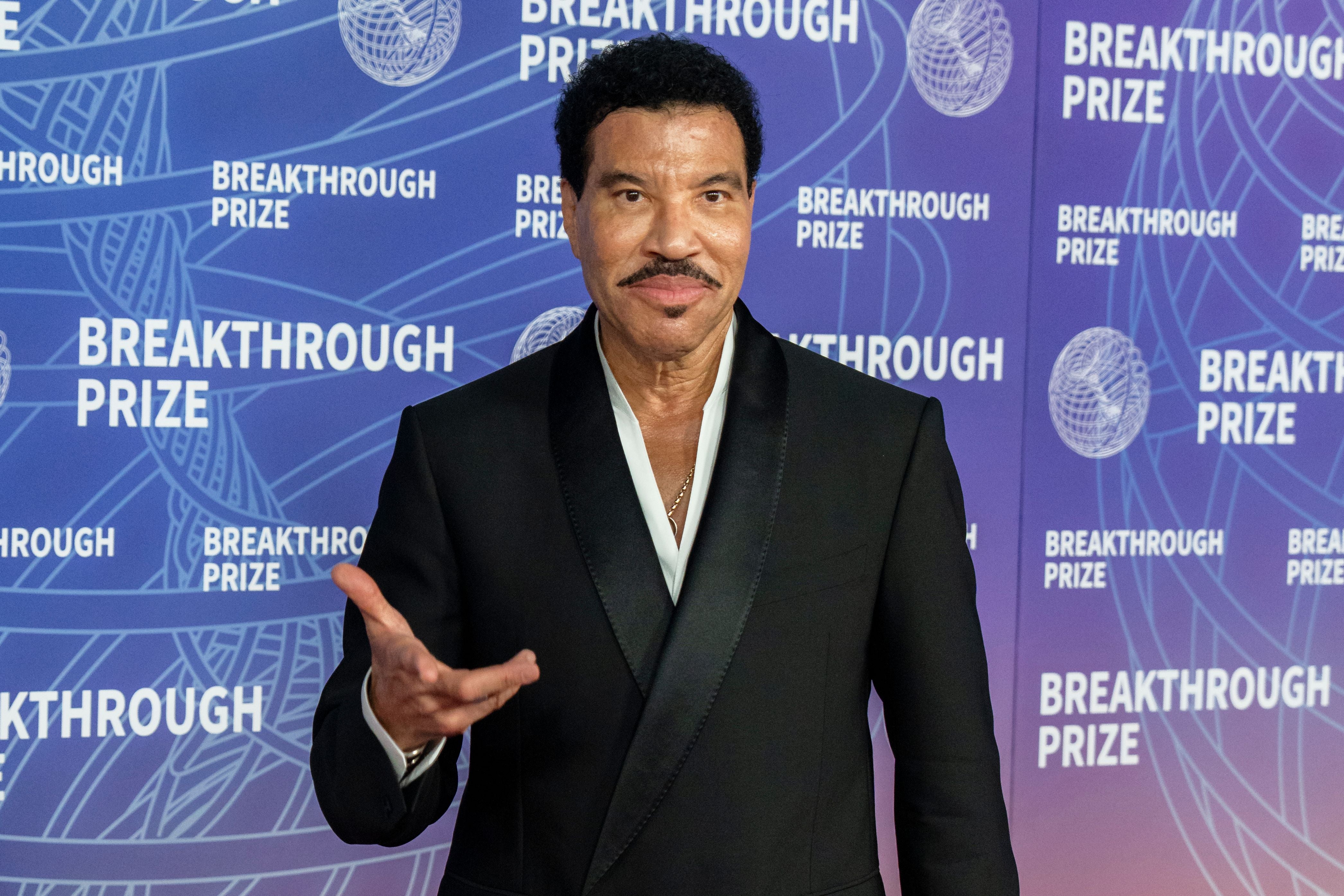 Ein Mann im schwarzen Anzug posiert lächelnd bei der Breakthrough Prize Zeremonie vor Fotowand.