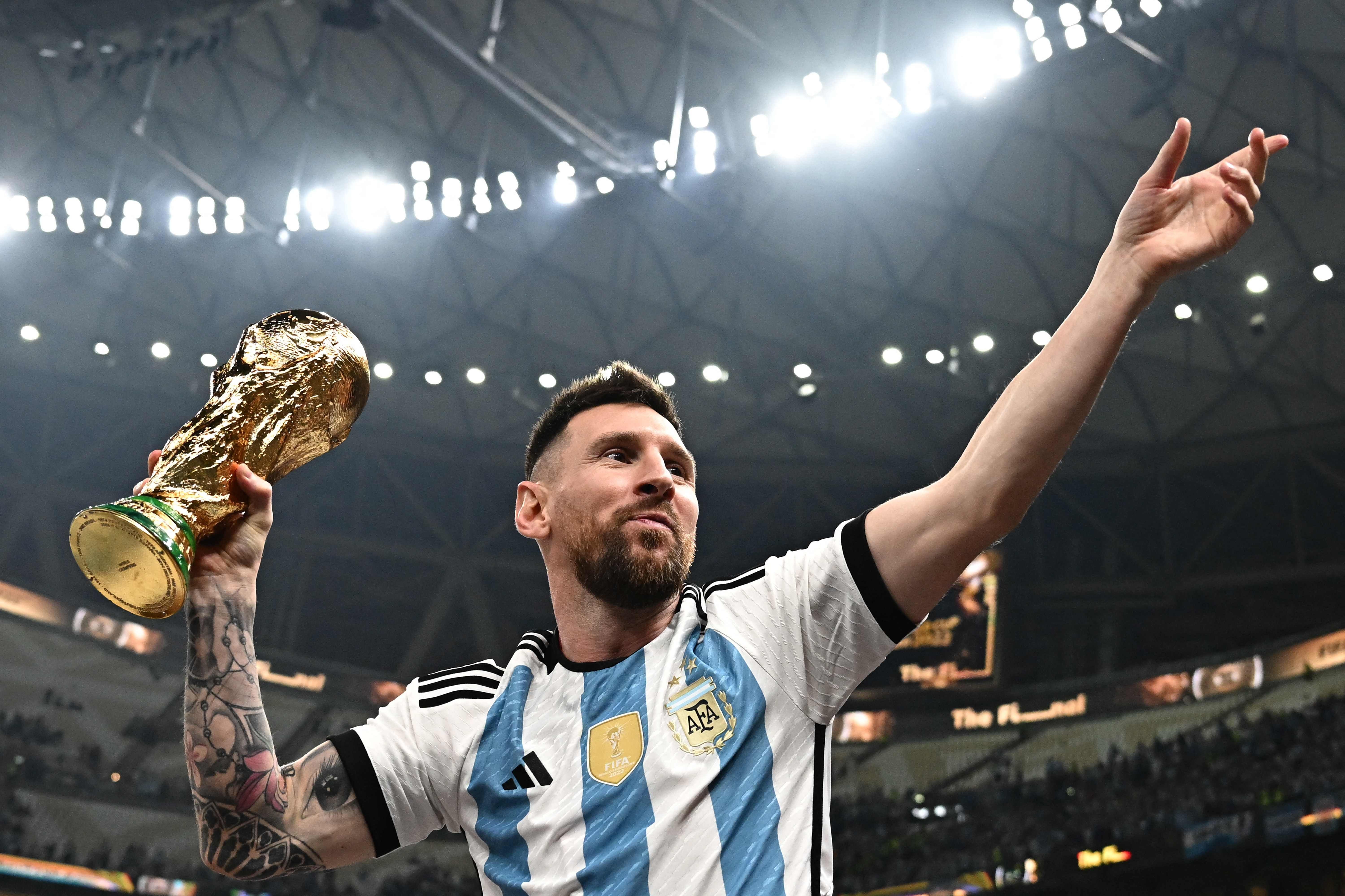 Ein Fußballspieler im argentinischen Trikot hält den WM-Pokal und jubelt im Stadion.