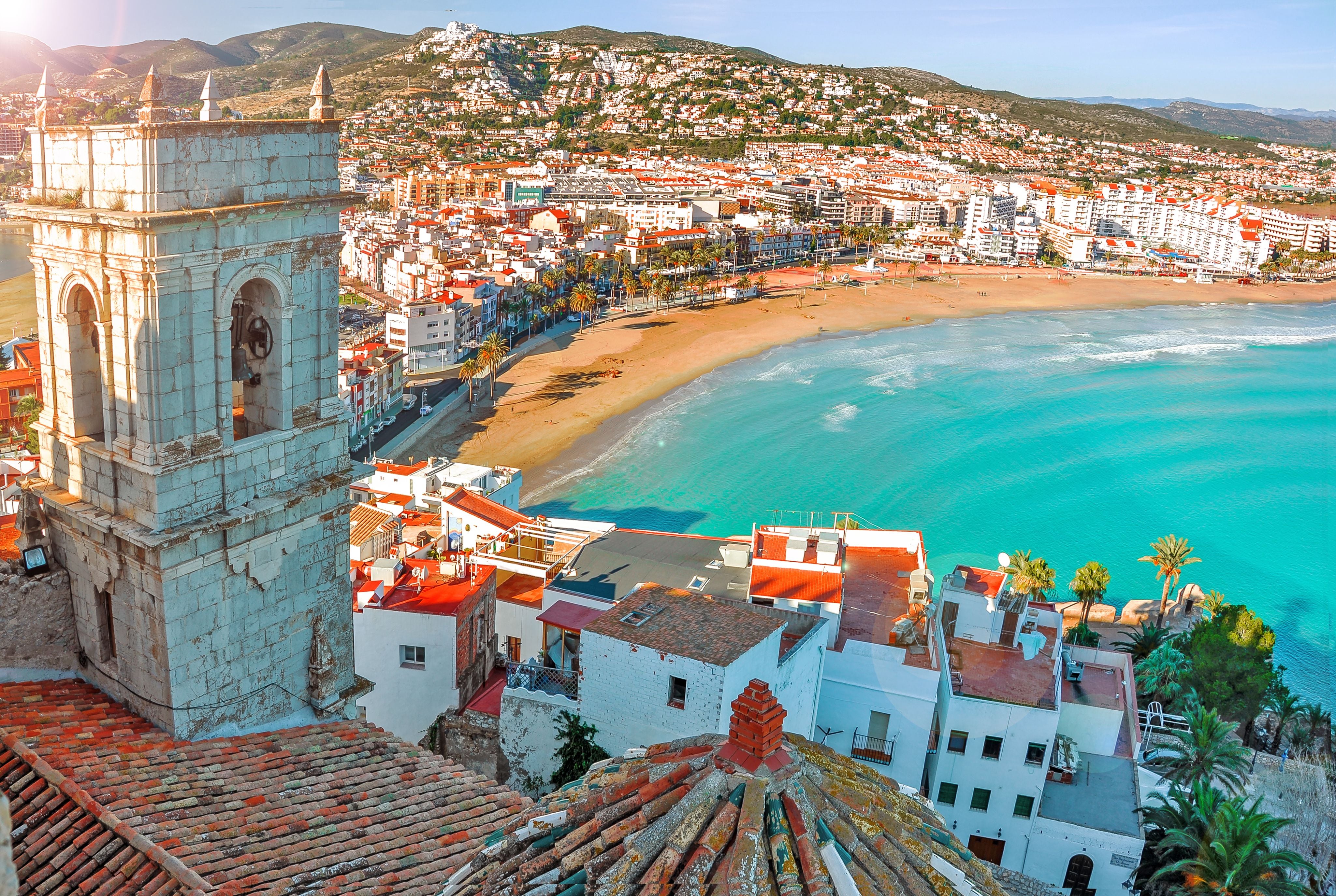 Blick über die Bucht von Peñíscola mit Strand, türkisfarbenem Meer und alten Gebäuden.