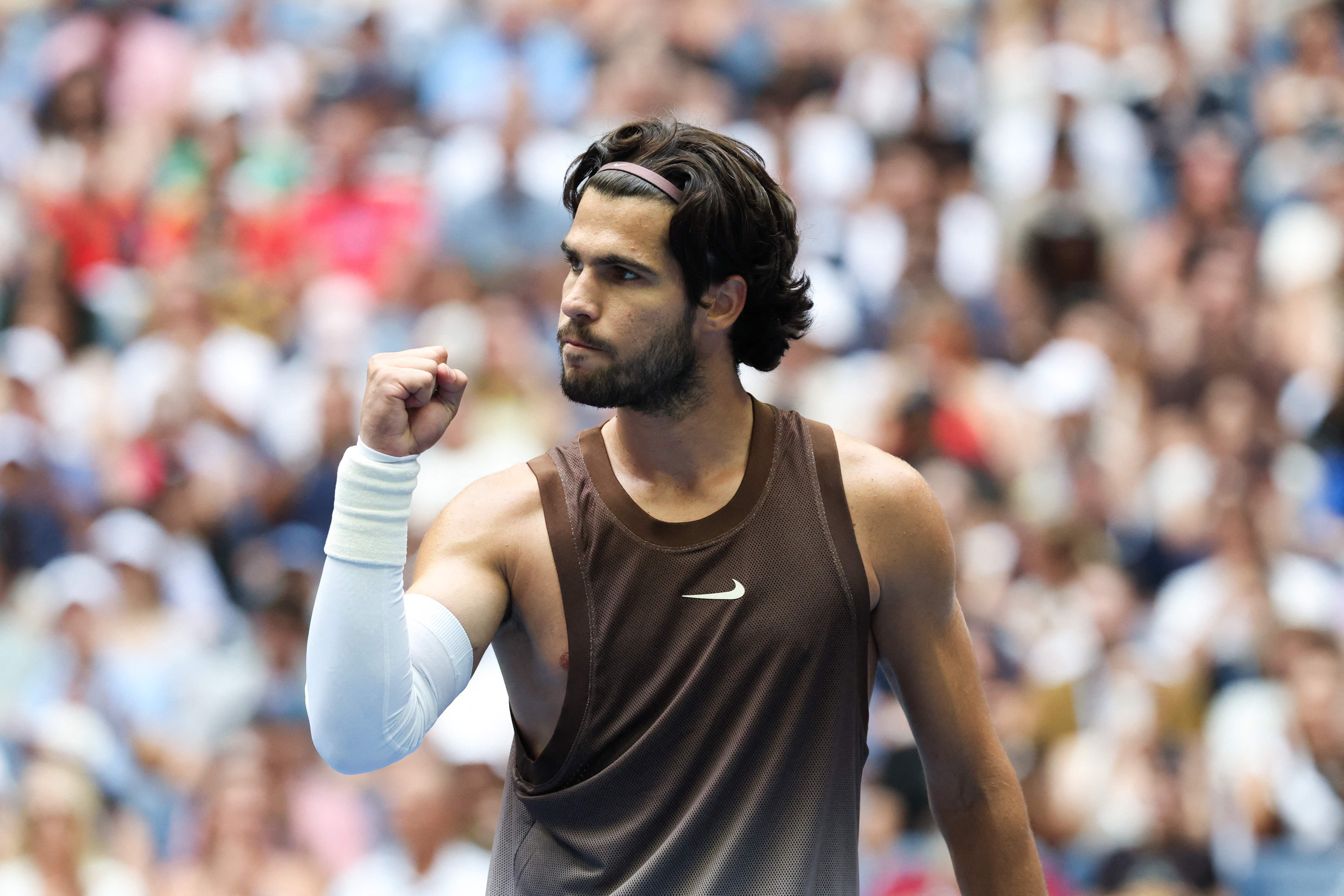 Tennisspieler hebt die Faust zum Jubel bei einem Match vor unscharfem Publikum.