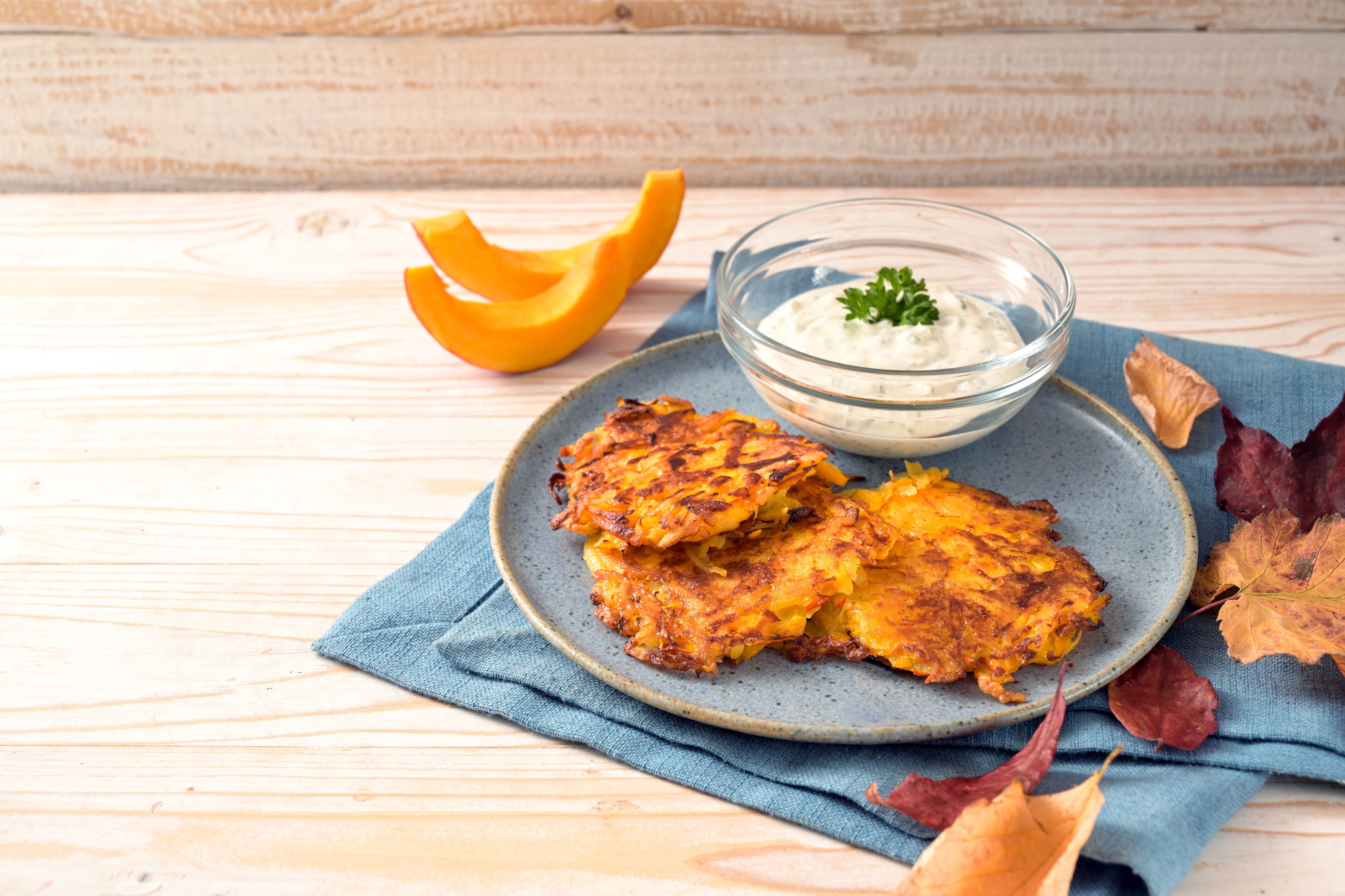 Kürbis-Kartoffel-Puffer mit Quark-Dip auf blauem Teller, herbstlich dekoriert.
