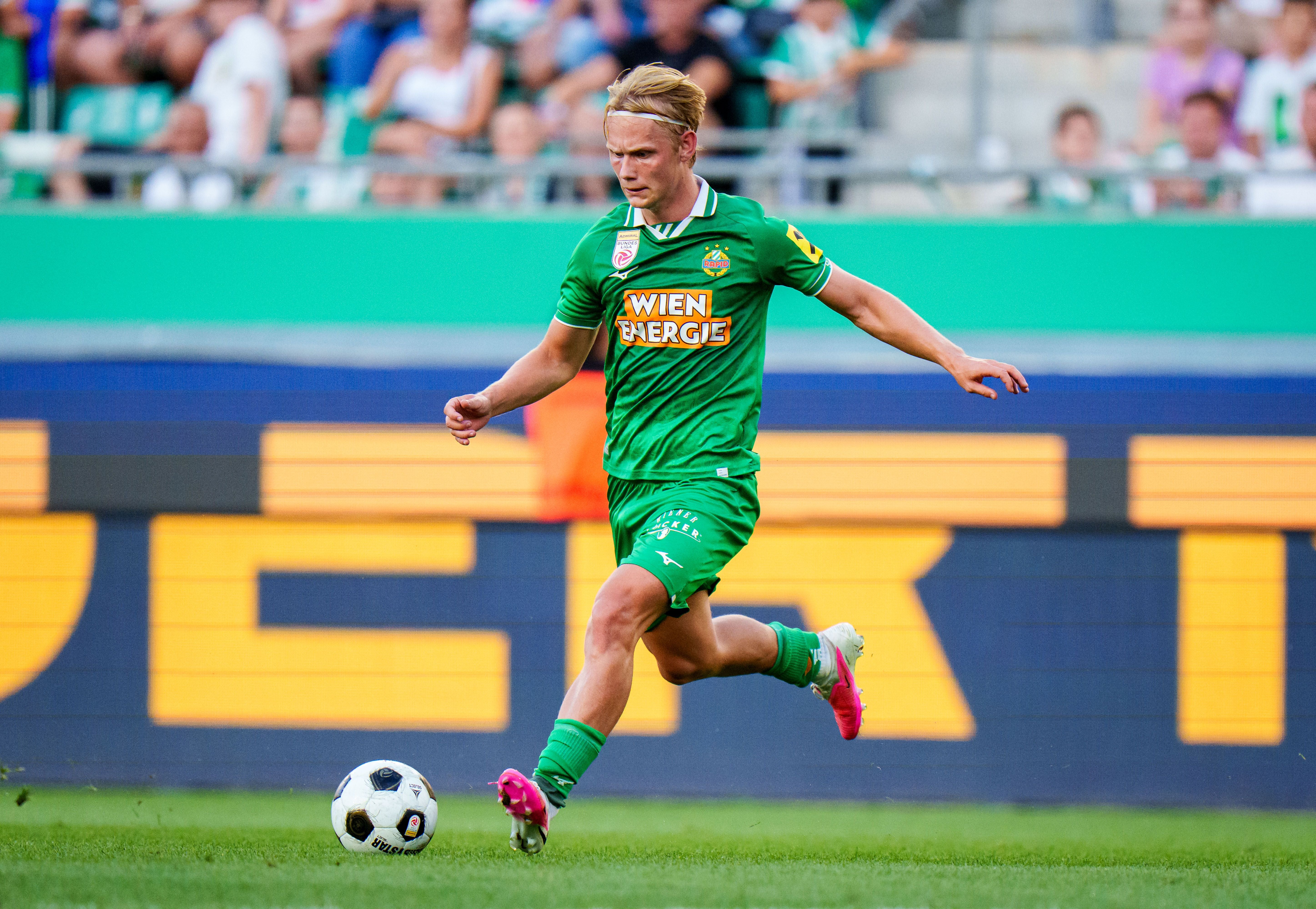 Ein Fußballspieler von Rapid Wien läuft während eines Spiels mit dem Ball am Spielfeld.