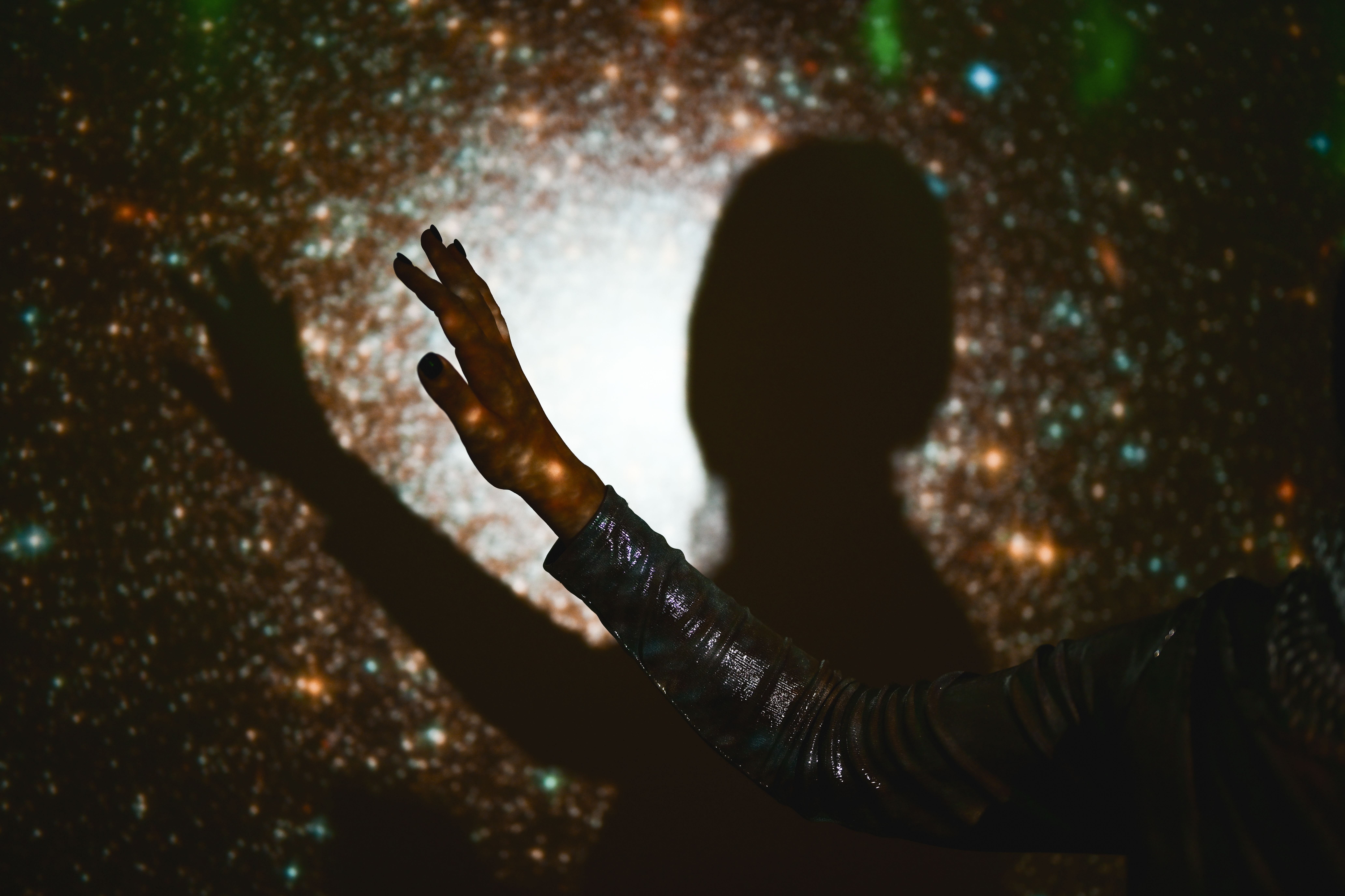 Hand und Schatten einer Person vor einem galaktischen Sternenhintergrund mit vielen Lichtpunkten.