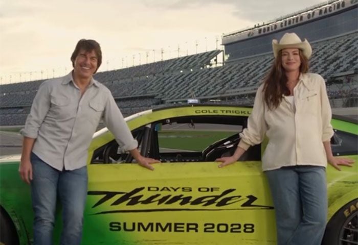 Ein Mann und eine Frau lehnen lächelnd an einem Rennwagen mit der Aufschrift "Days of Thunder".
