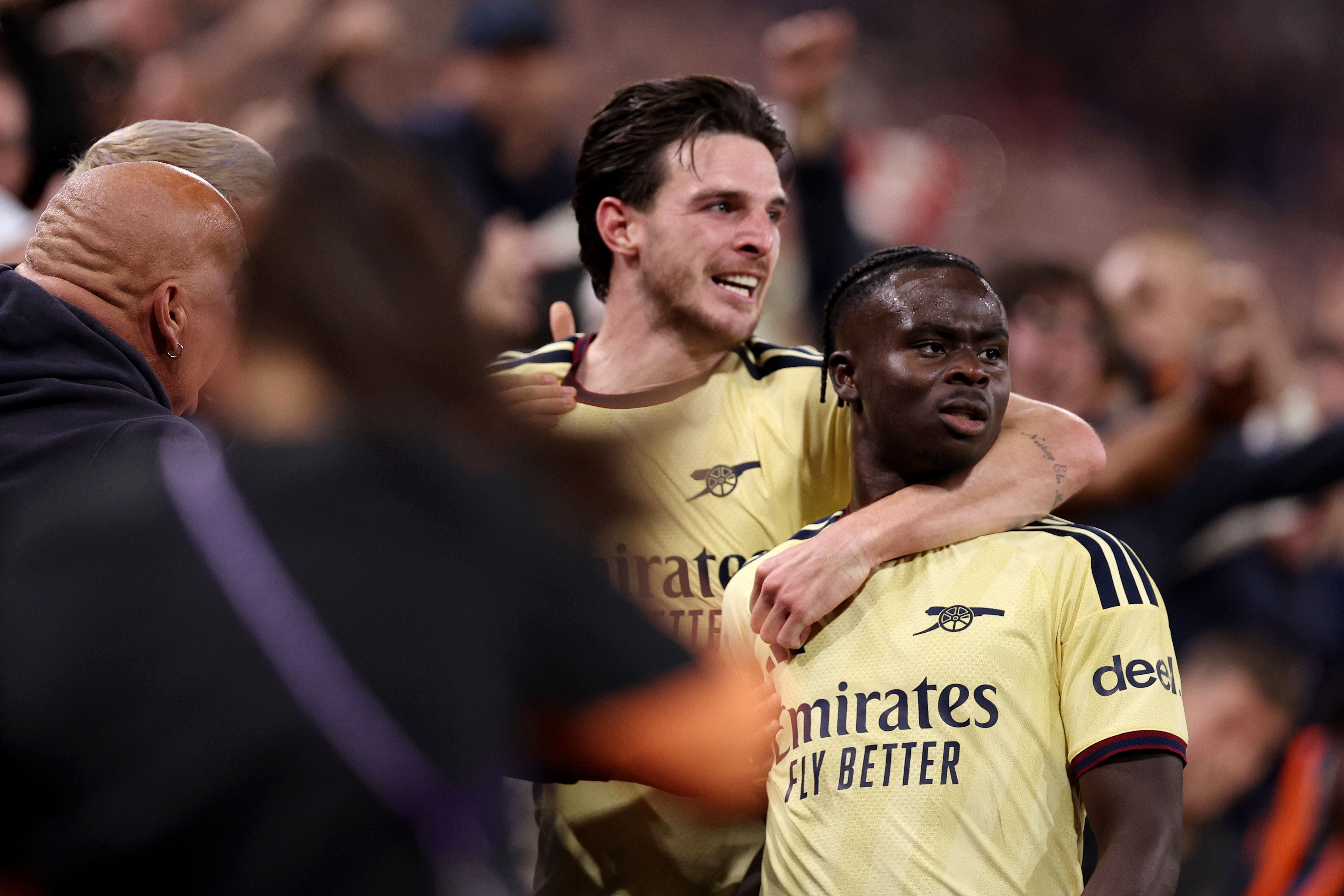 Zwei Arsenal-Spieler jubeln auf dem Spielfeld nach einem Tor, Fans feiern im Hintergrund.