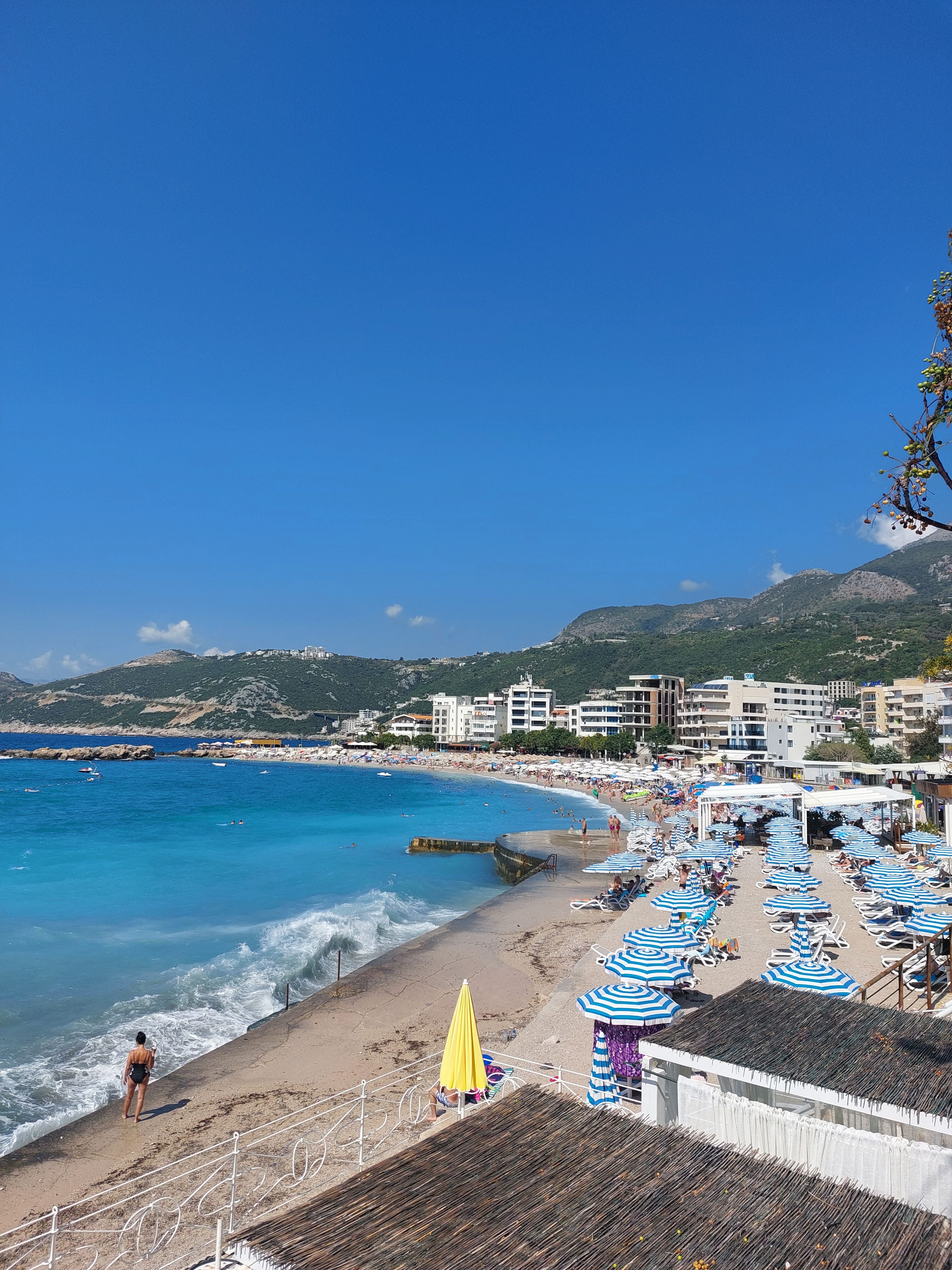 Strand mit Sonnenschirmen, blauem Meer und Bergen im Hintergrund in Dobra Voda, Montenegro.