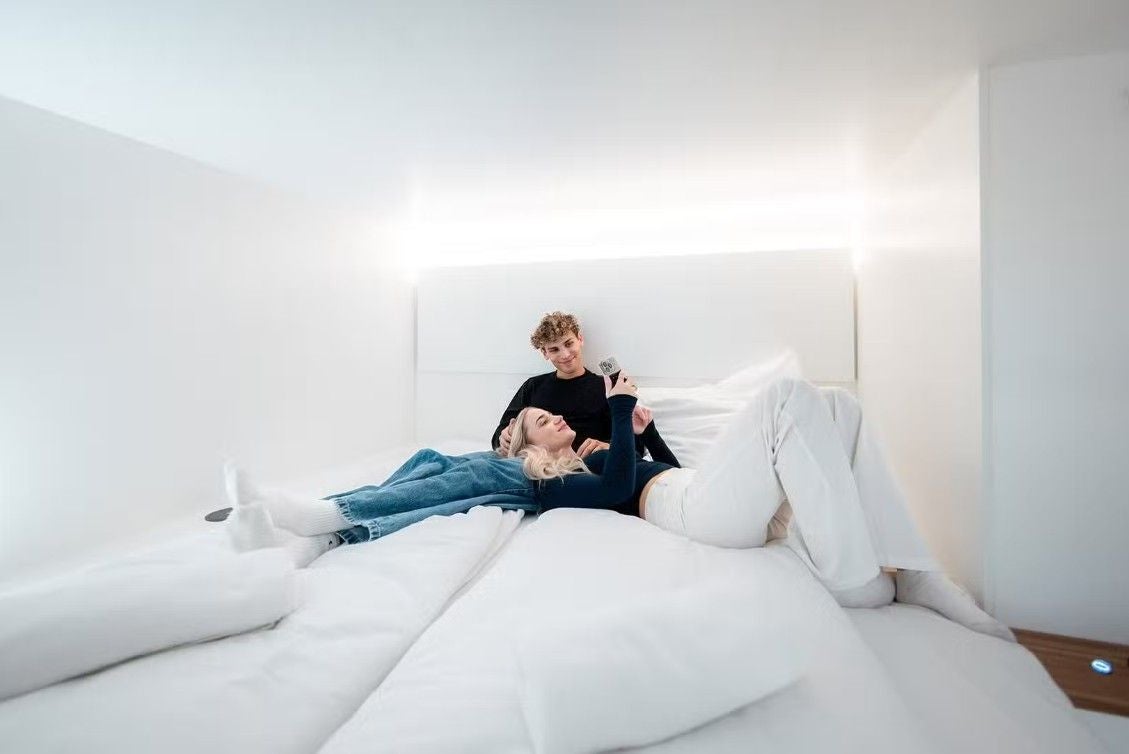 Zwei Personen entspannen gemeinsam auf einem großen, weißen Bett in einem modernen Hotelzimmer.