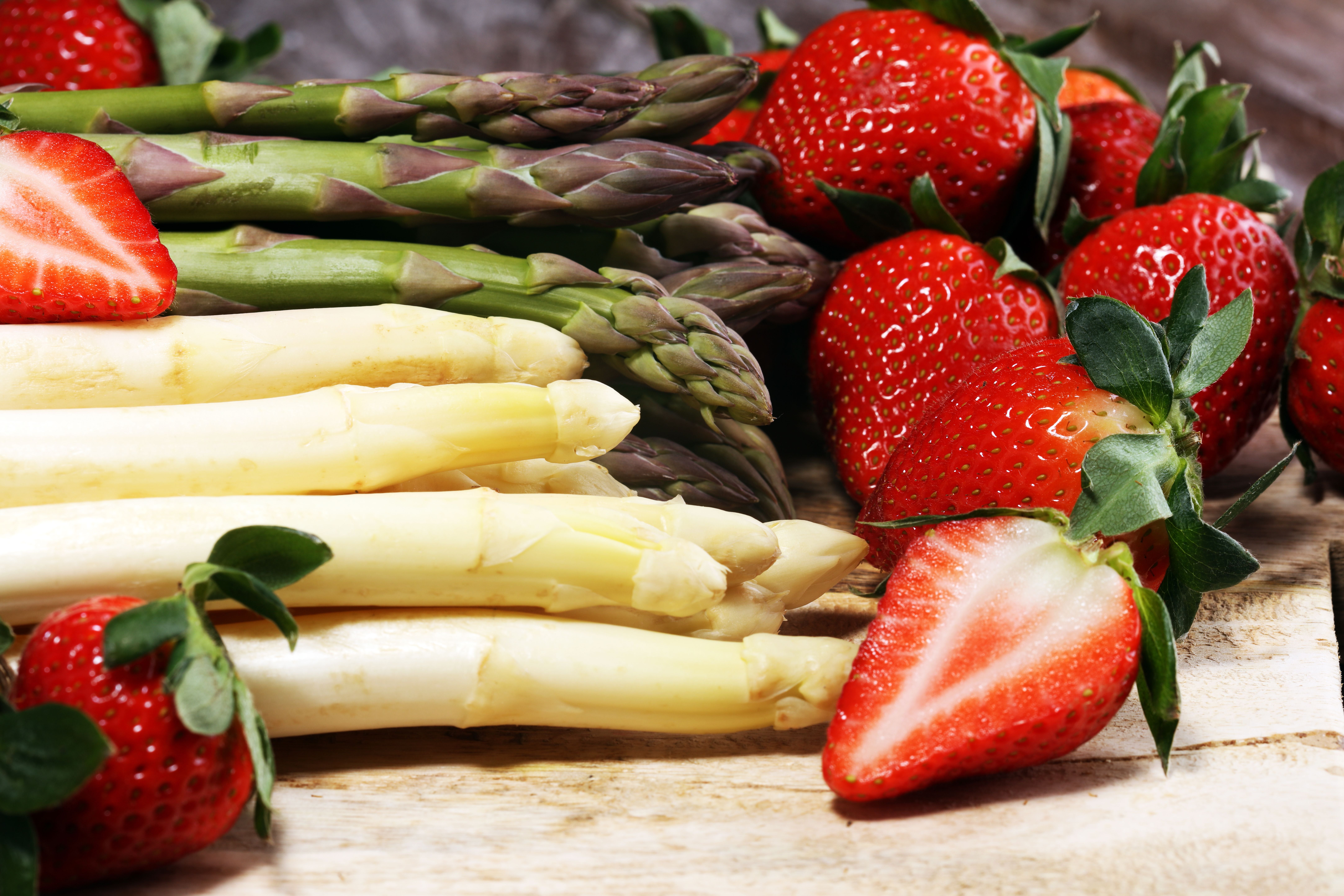 Weißer und grüner Spargel liegen neben frischen Erdbeeren auf einem Holztisch.
