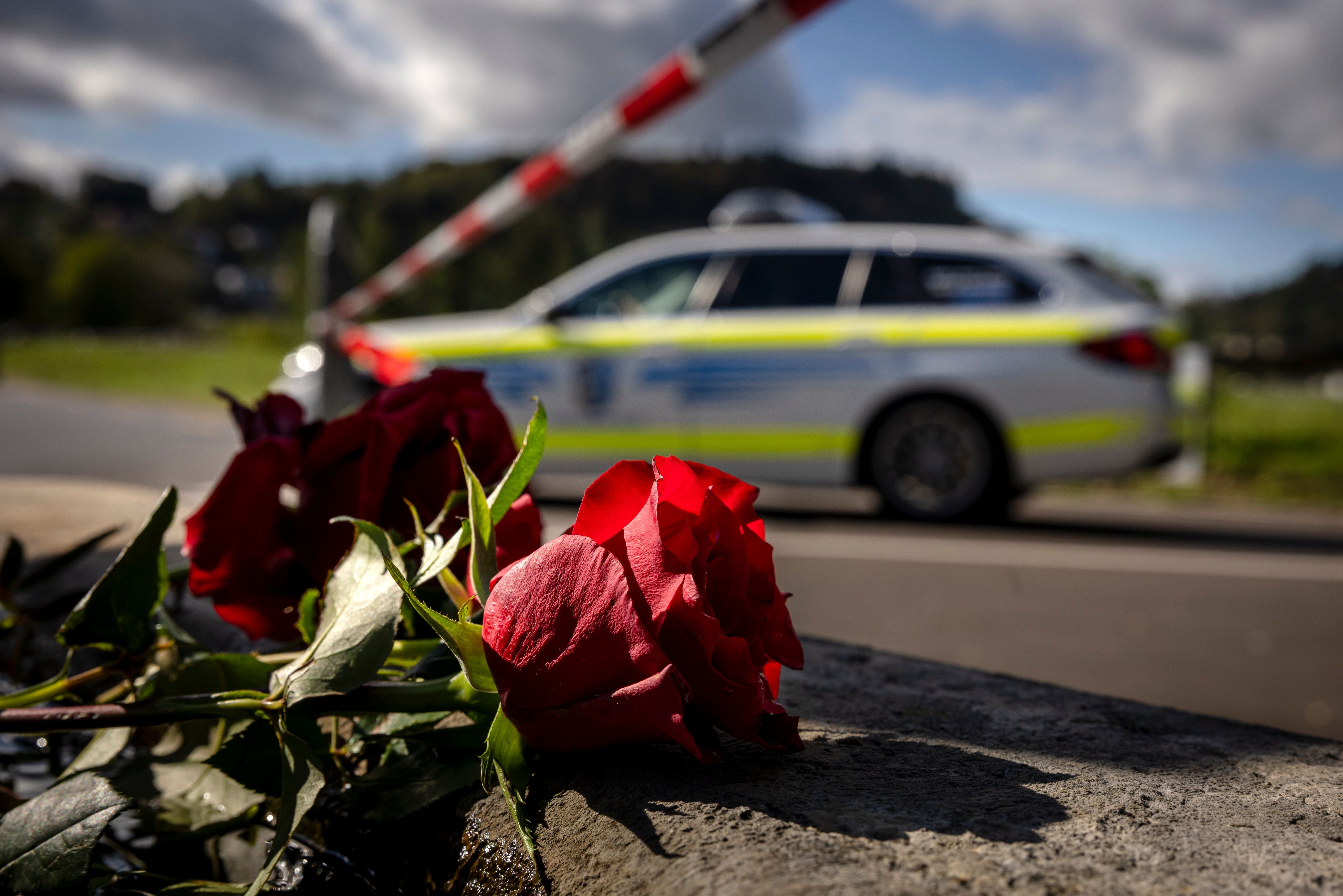 Rote Rosen liegen am Straßenrand, im Hintergrund ein Polizeiauto und eine Absperrung.