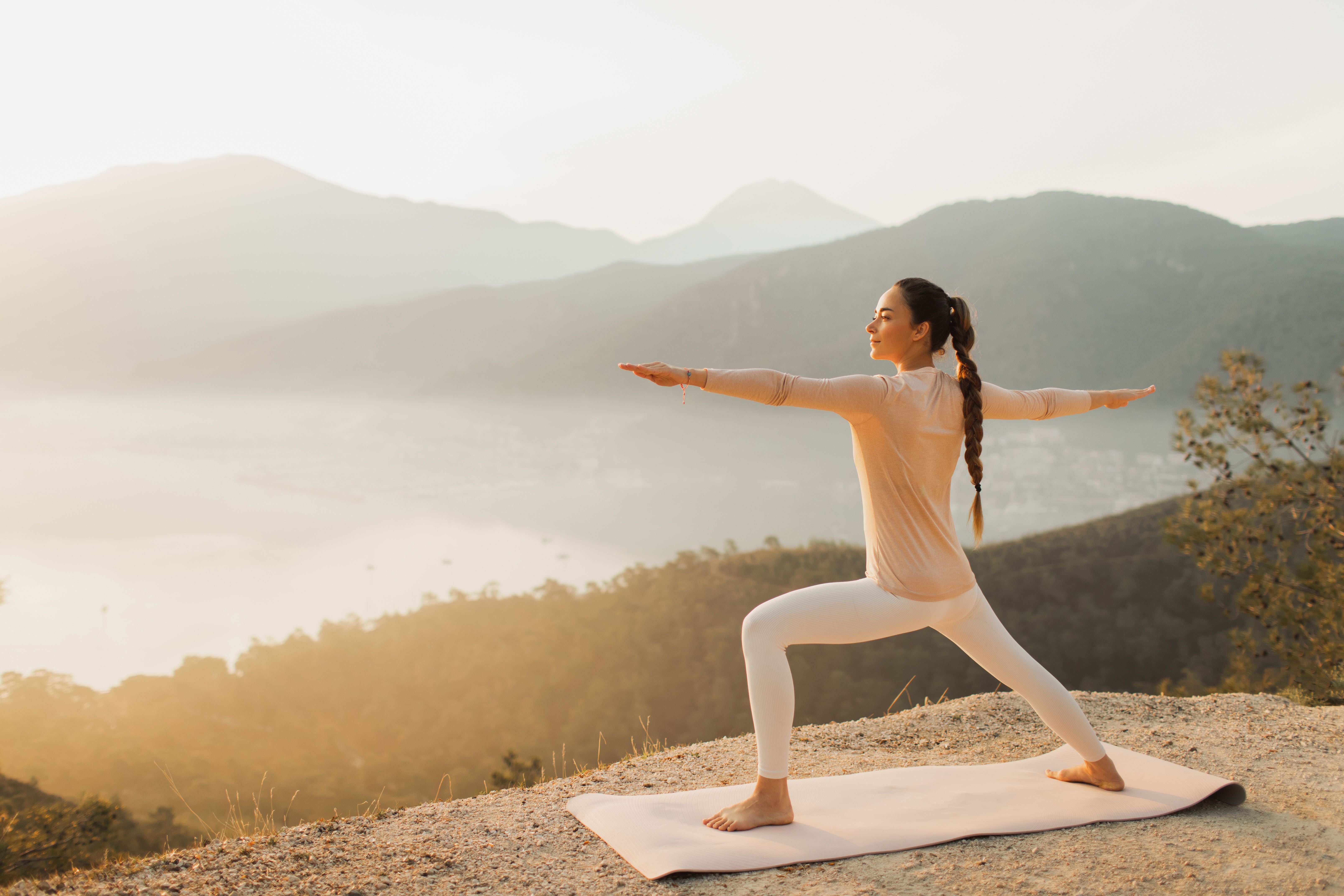 Frau macht Yoga auf Matte, mit Blick auf neblige Berge und eine Bucht im Hintergrund.