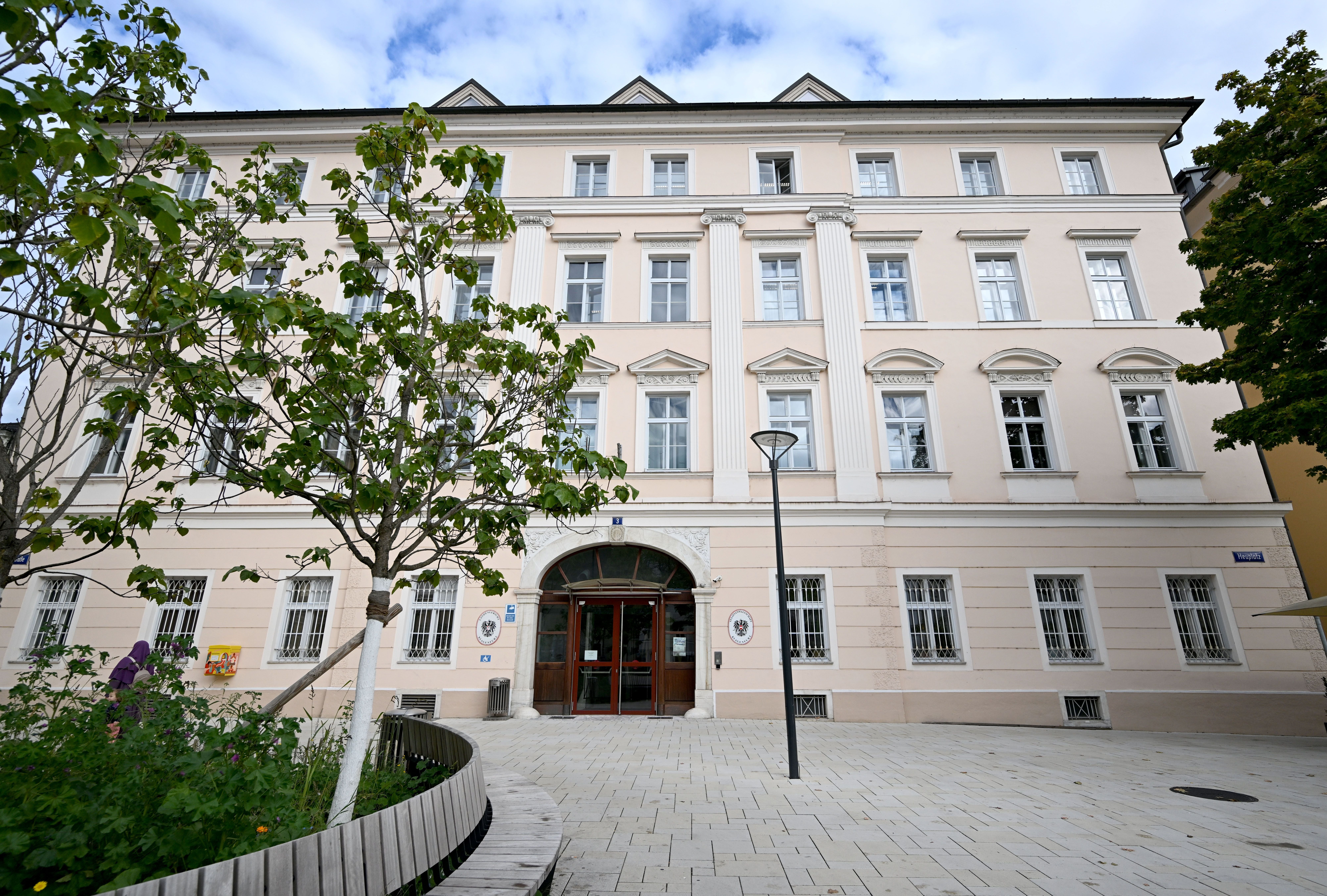 Das Justizzentrum Klagenfurt mit hellem Fassadenanstrich und Bäumen im Vordergrund.