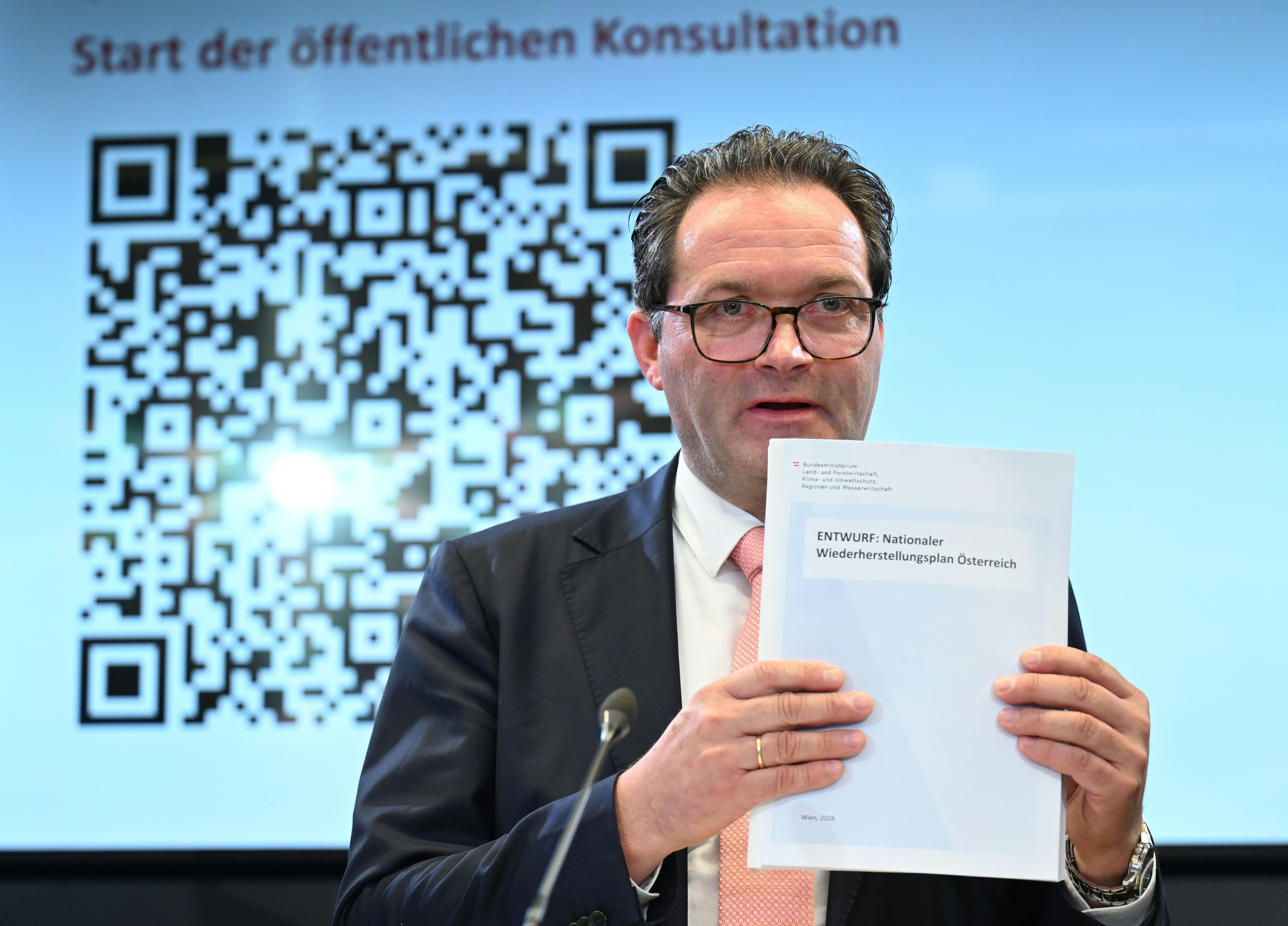 Ein Mann hält ein Dokument vor einem großen QR-Code und einem Text zur öffentlichen Konsultation.