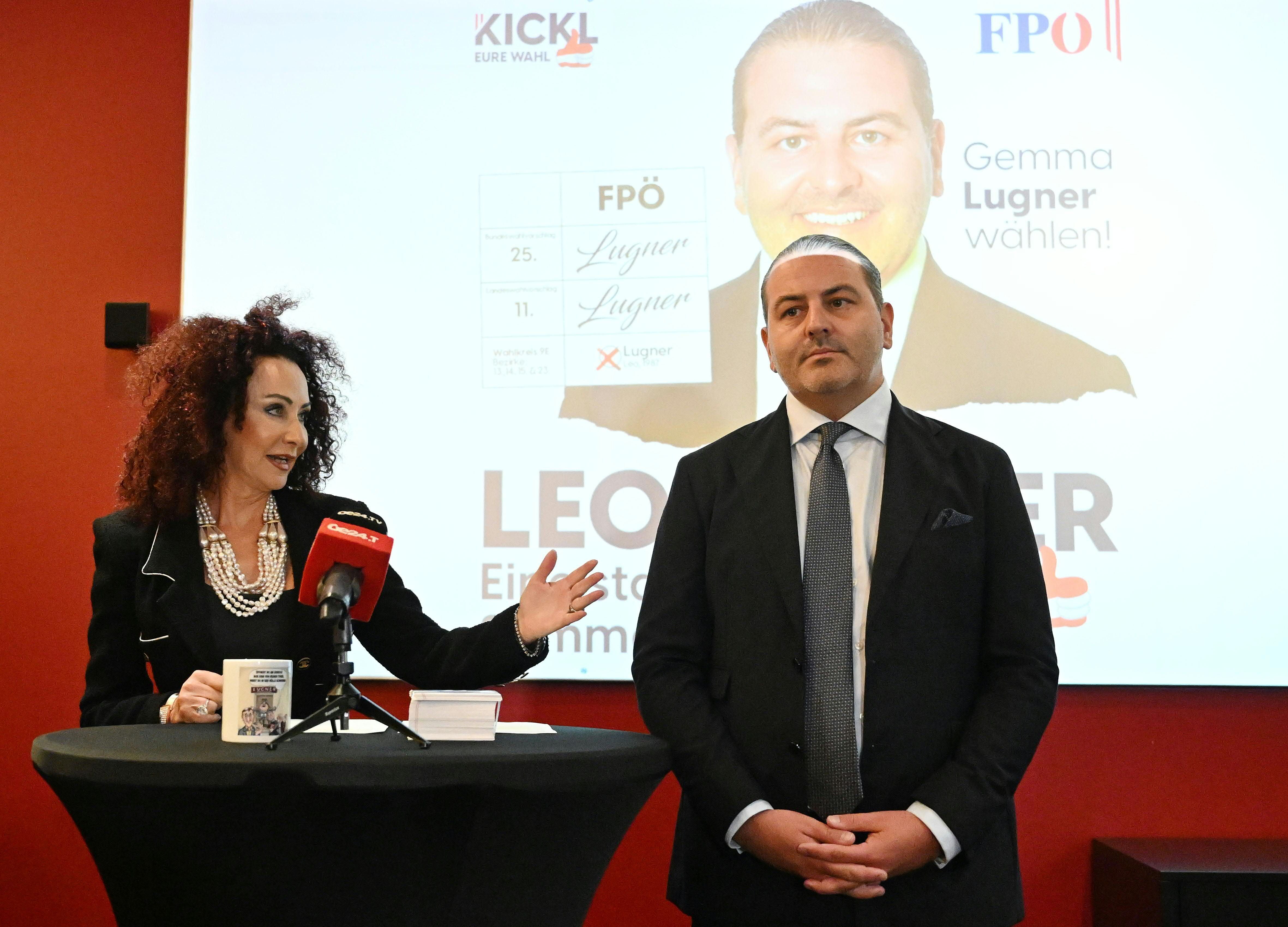 Christina Lugner spricht am Tisch, Leo Lugner steht daneben vor einem Wahlplakat in Wien.
