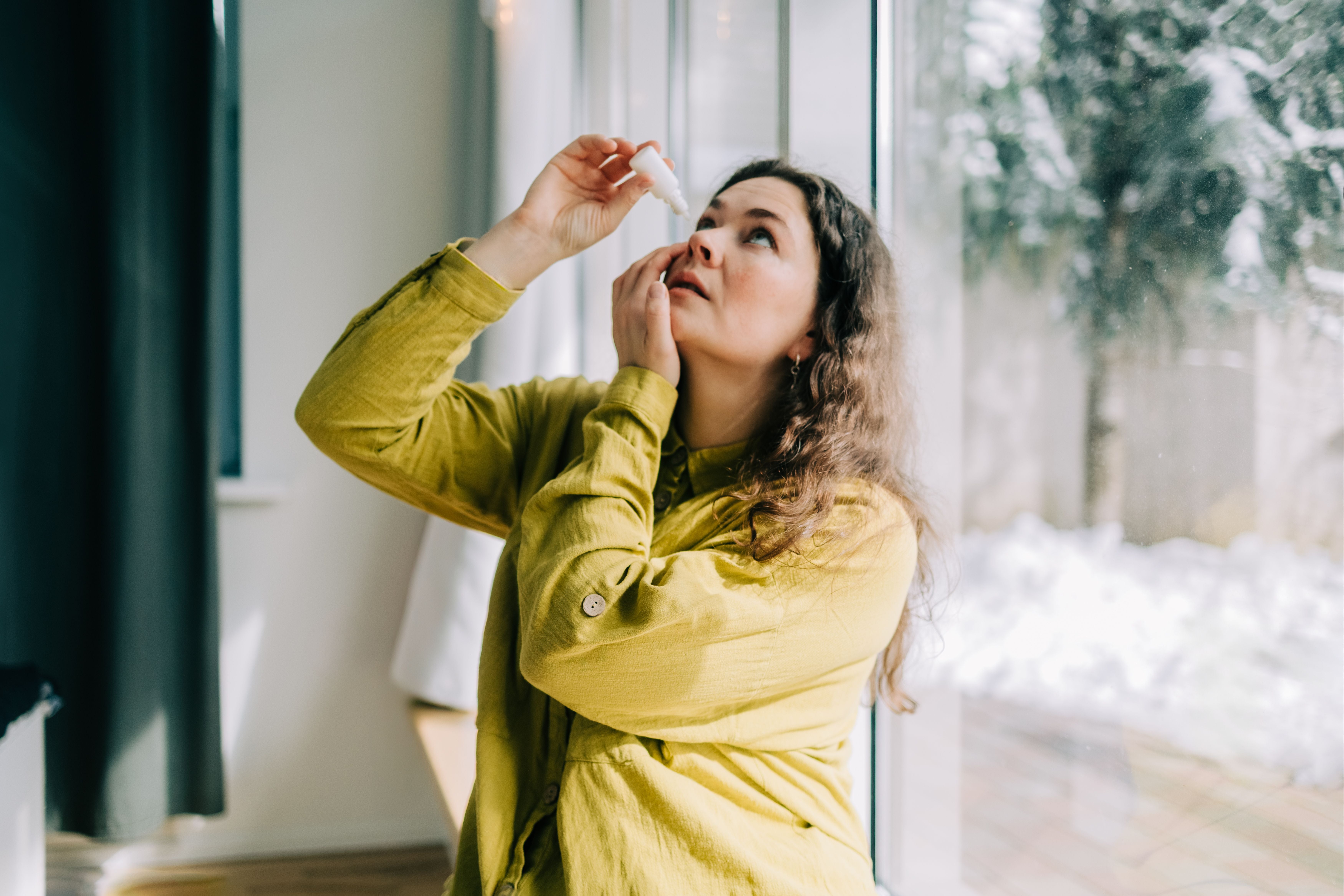 Frau träufelt sich zu Hause im Winter Augentropfen ins Auge.