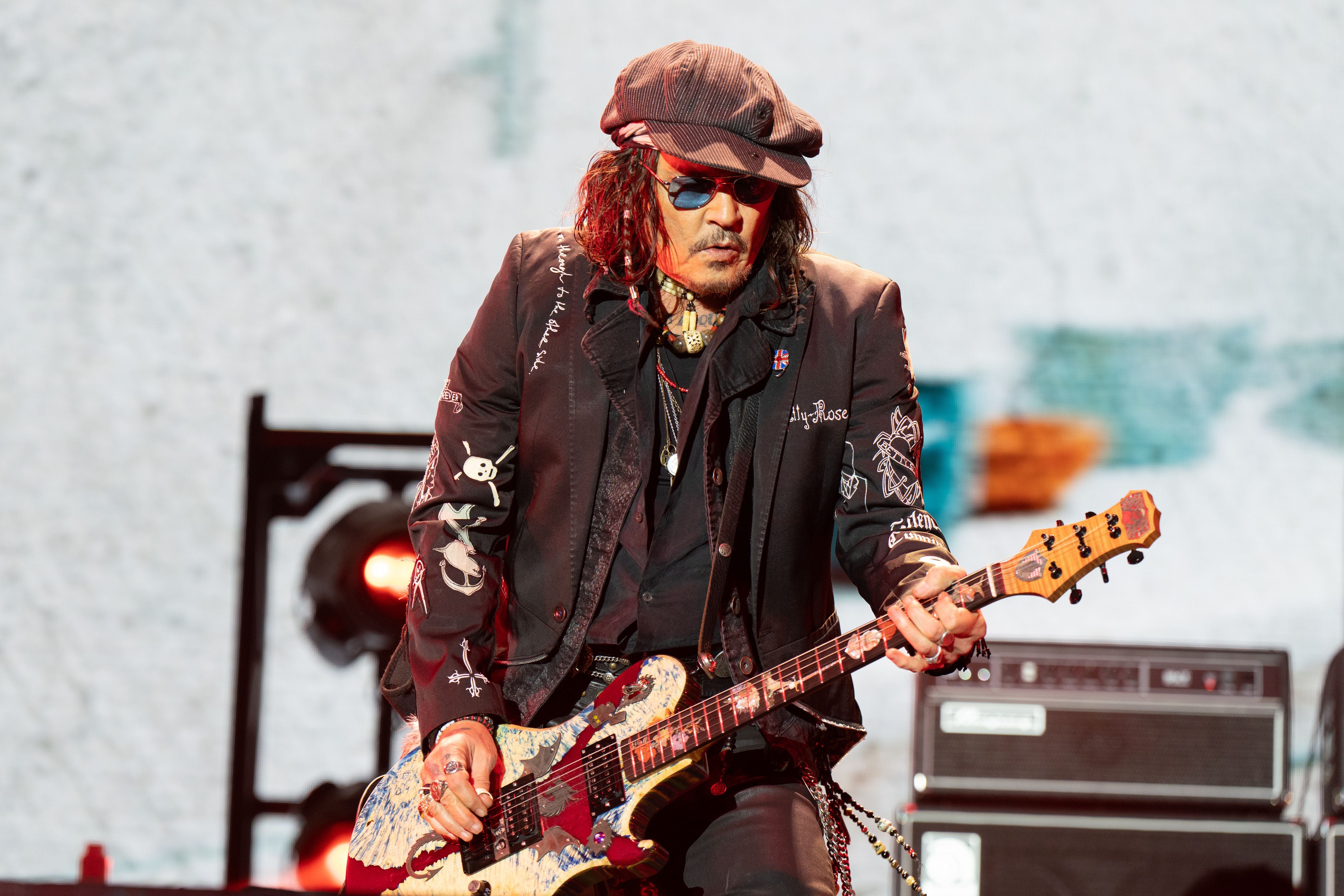 Rockmusiker spielt E-Gitarre auf einer Bühne, trägt Sonnenbrille und Mütze.
