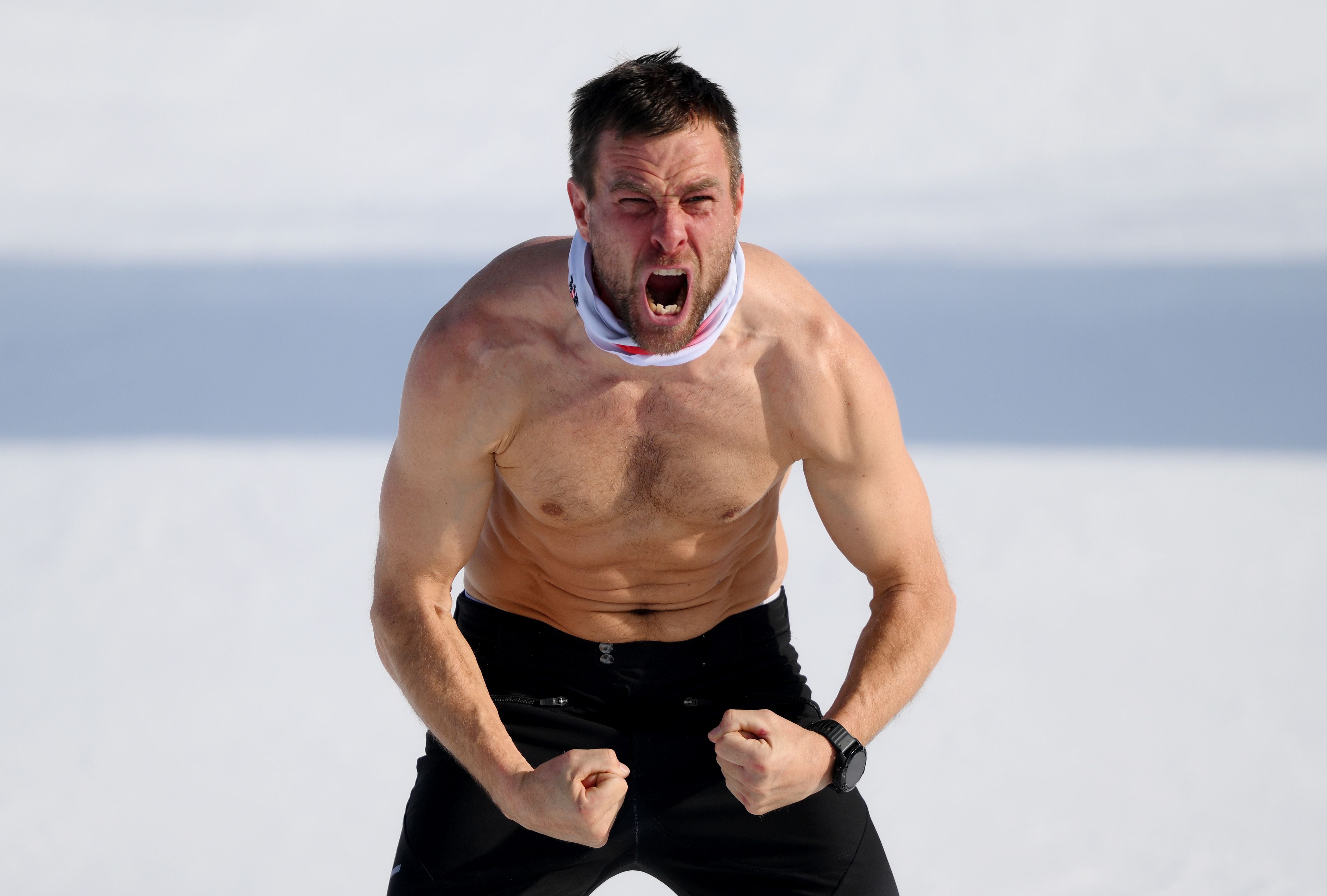 Ein oberkörperfreier Mann jubelt mit geballten Fäusten im Schnee.