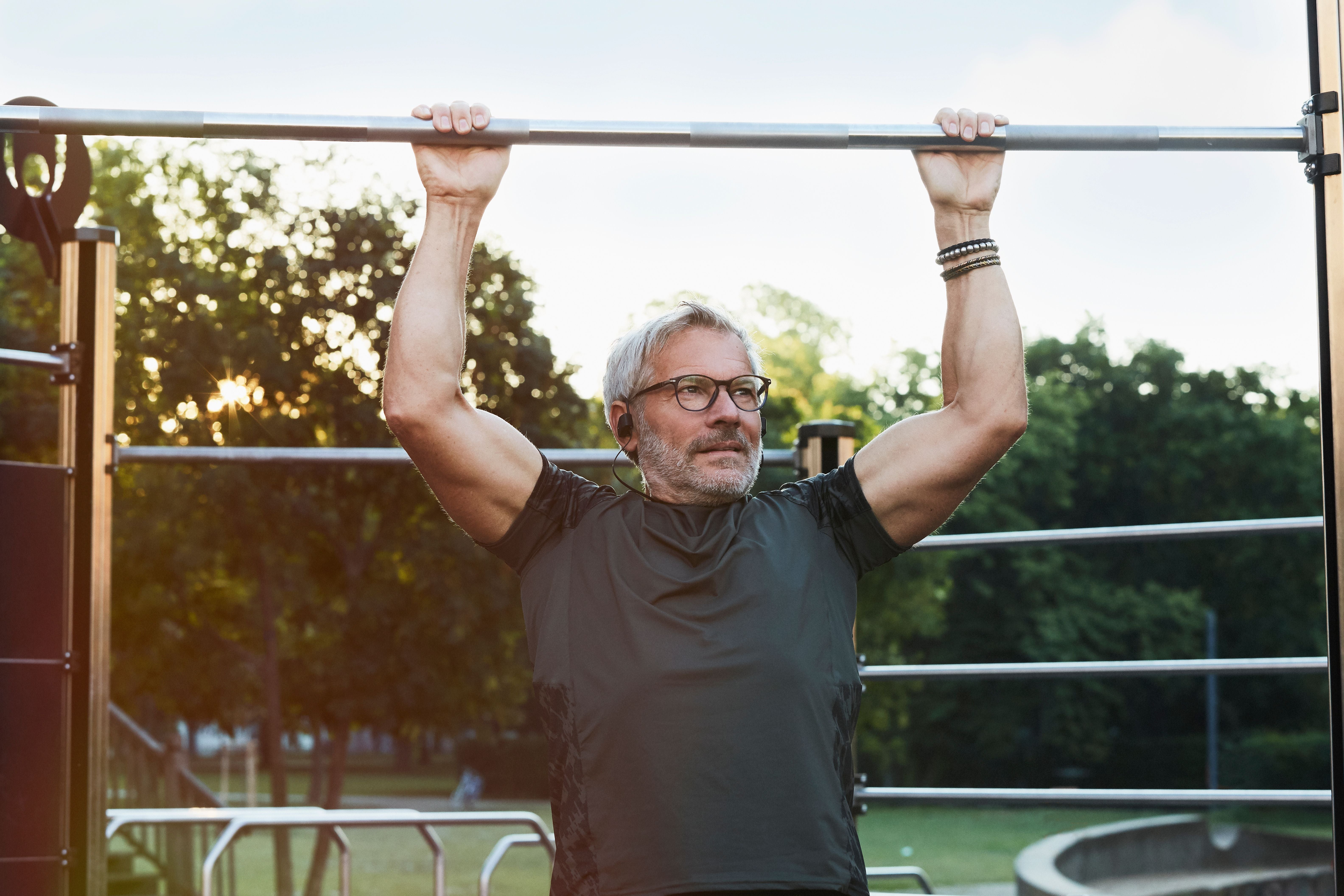 Älterer Mann trainiert an einer Klimmzugstange im Freien im Fitnesspark.