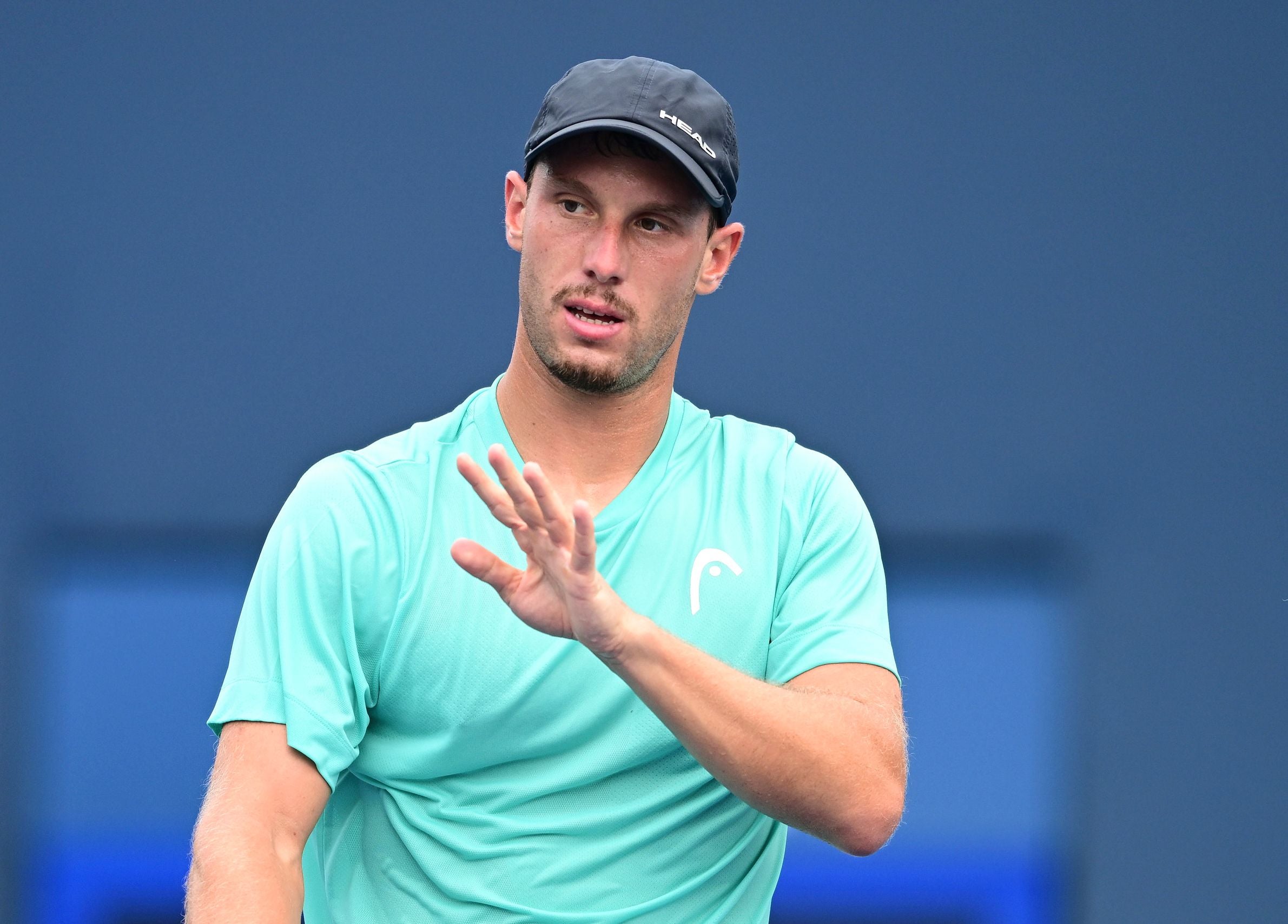 Ein Tennisspieler mit türkisfarbenem Shirt und schwarzer Kappe gestikuliert auf dem Platz.