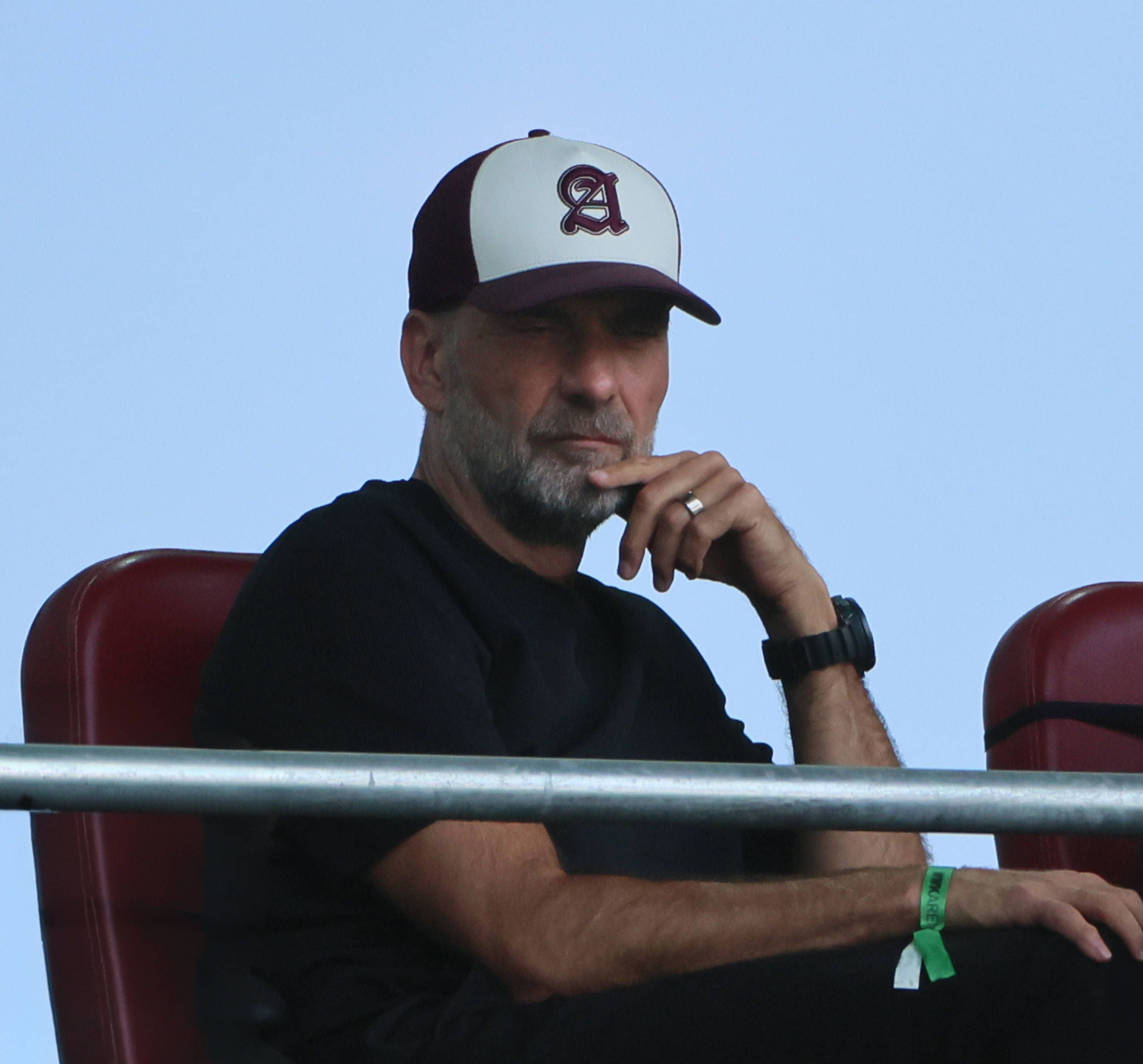 Ein Mann mit Bart und Basecap sitzt nachdenklich auf einem Stadionplatz.