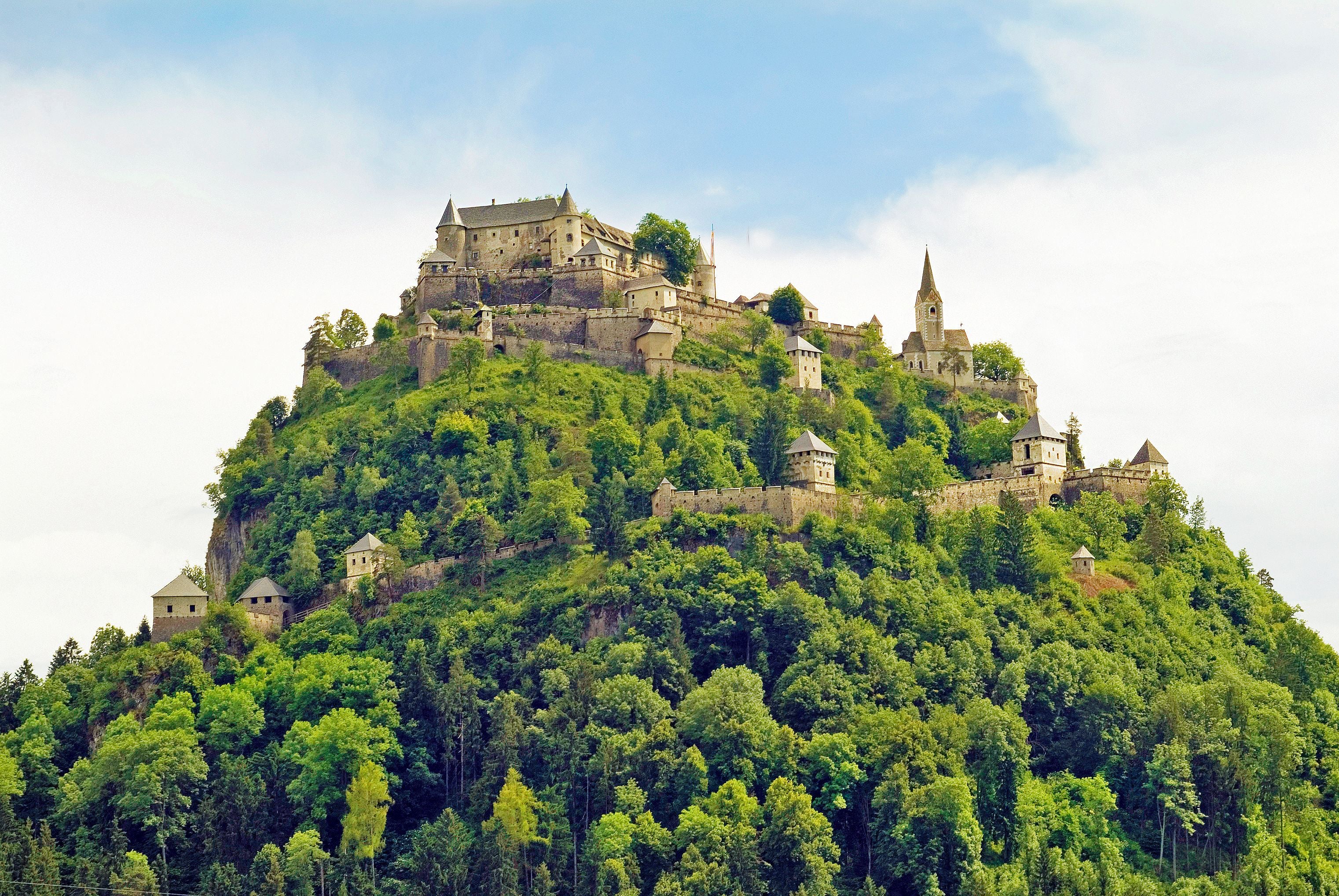 Burg Hochosterwitz thront auf einem bewaldeten Hügel unter blauem Himmel in Kärnten, Österreich.