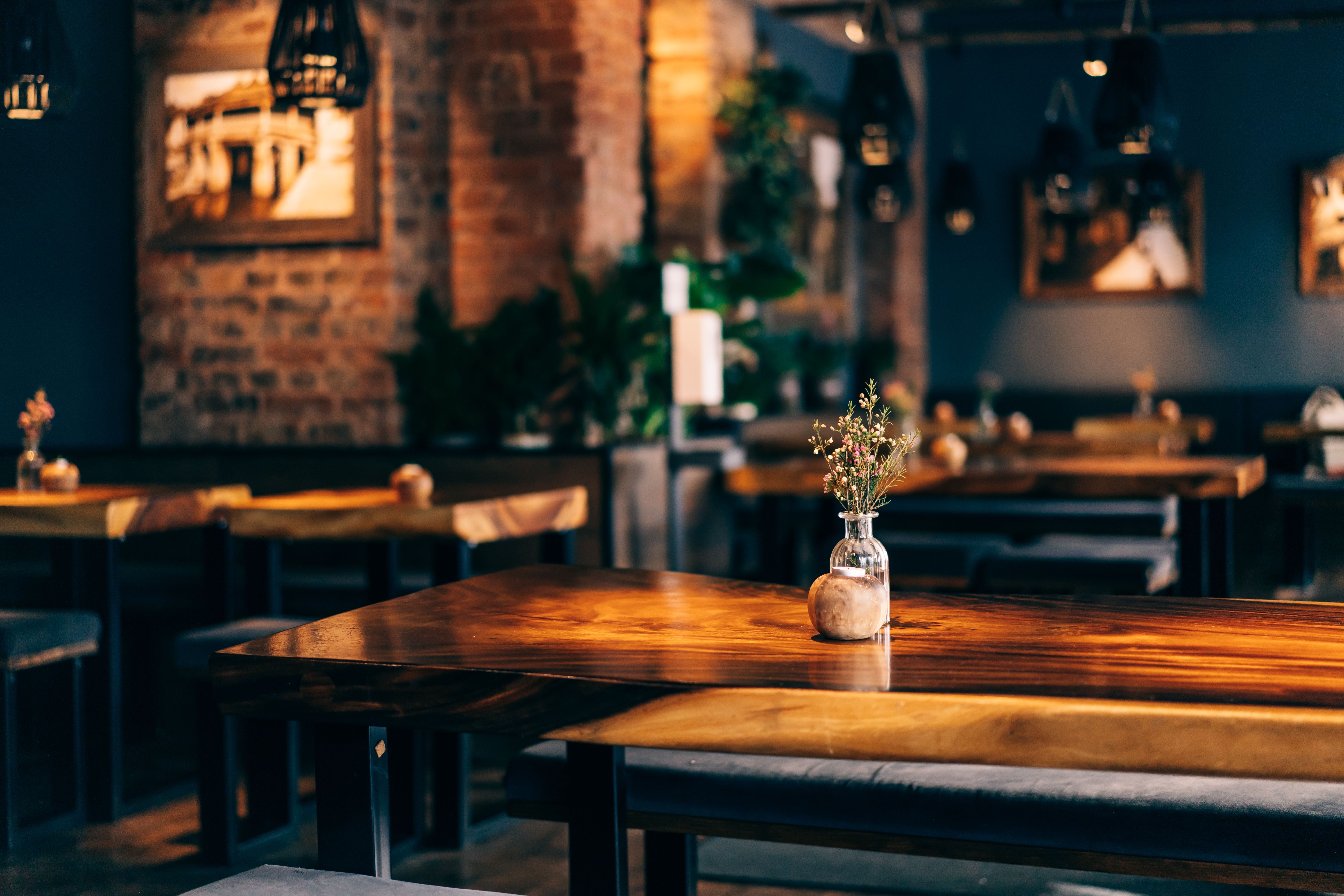 Gemütliches Café mit Holztischen, Blumenvasen und industriellem Stil in warmer Beleuchtung.
