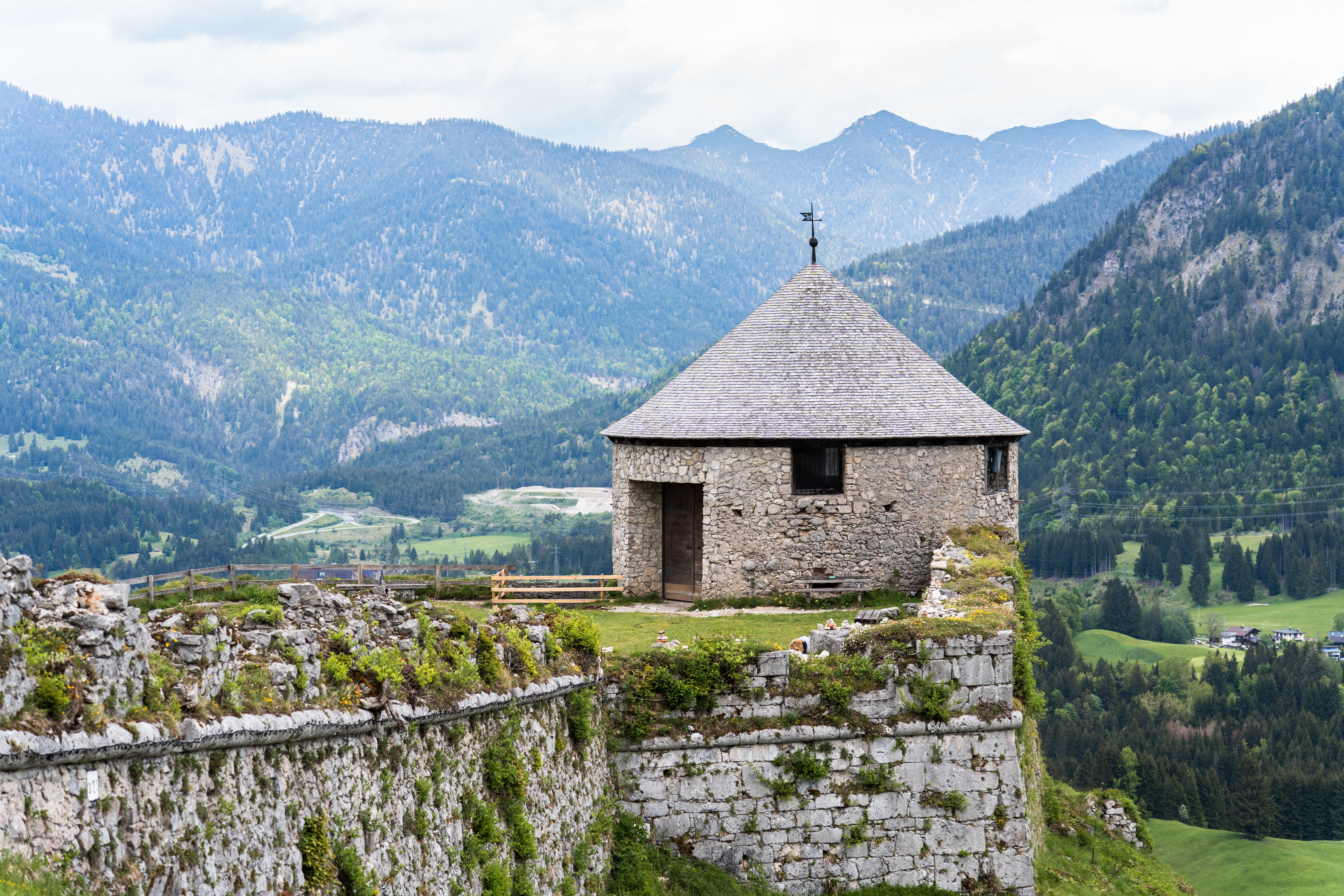 Runder Turm der Burg Ehrenberg mit Blick auf ein idyllisches Tiroler Tal und bewaldete Berge.