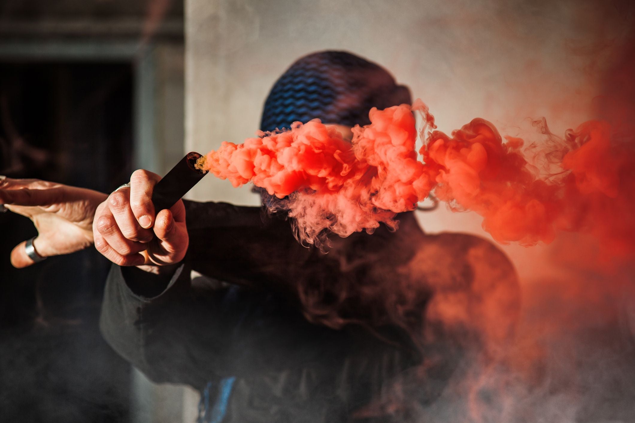 Person mit Mütze hält rote Rauchfackel, dichter Rauch verdeckt teilweise das Gesicht.