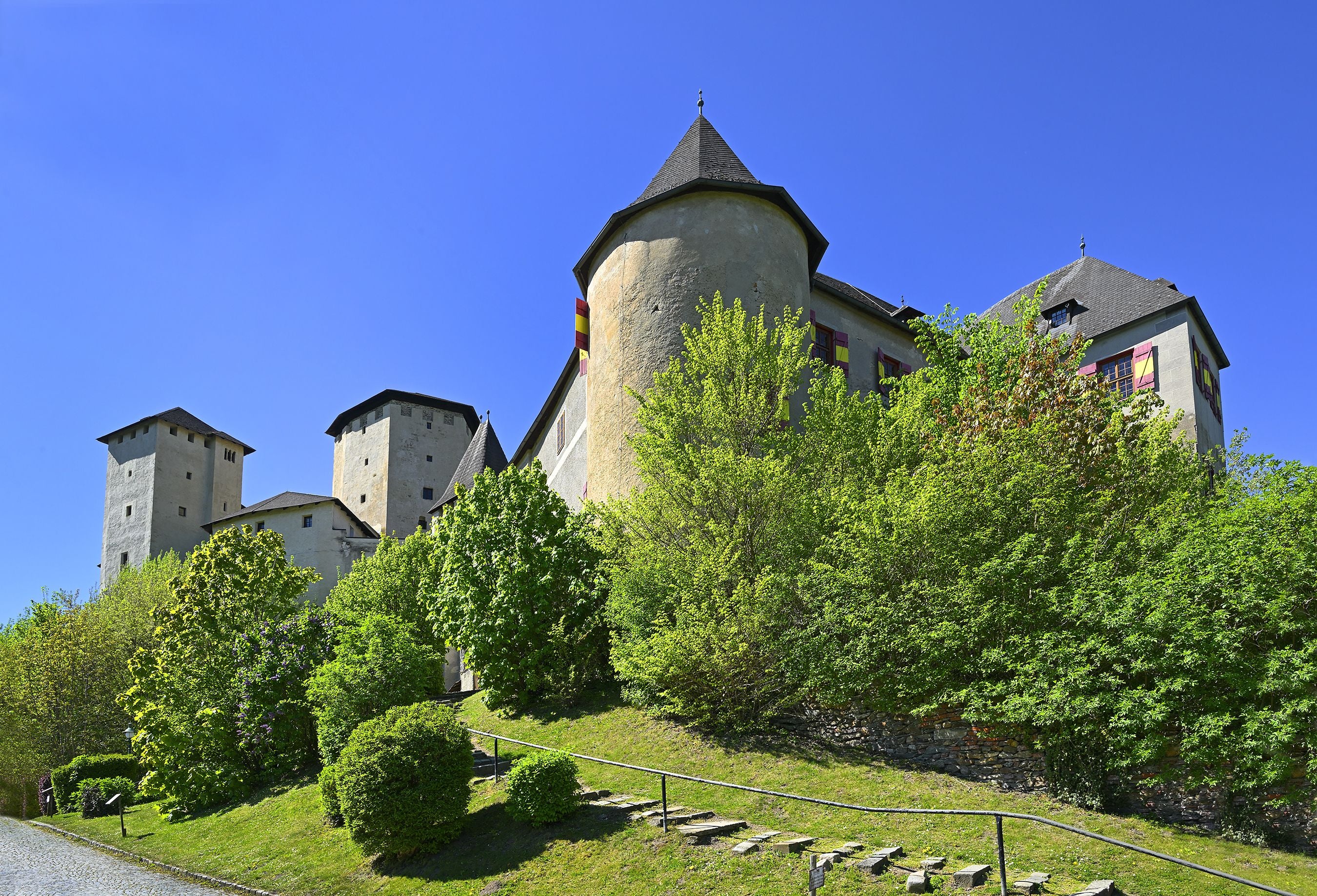 Burg Lockenhaus auf einem Hügel, umgeben von grünen Bäumen unter blauem Himmel.