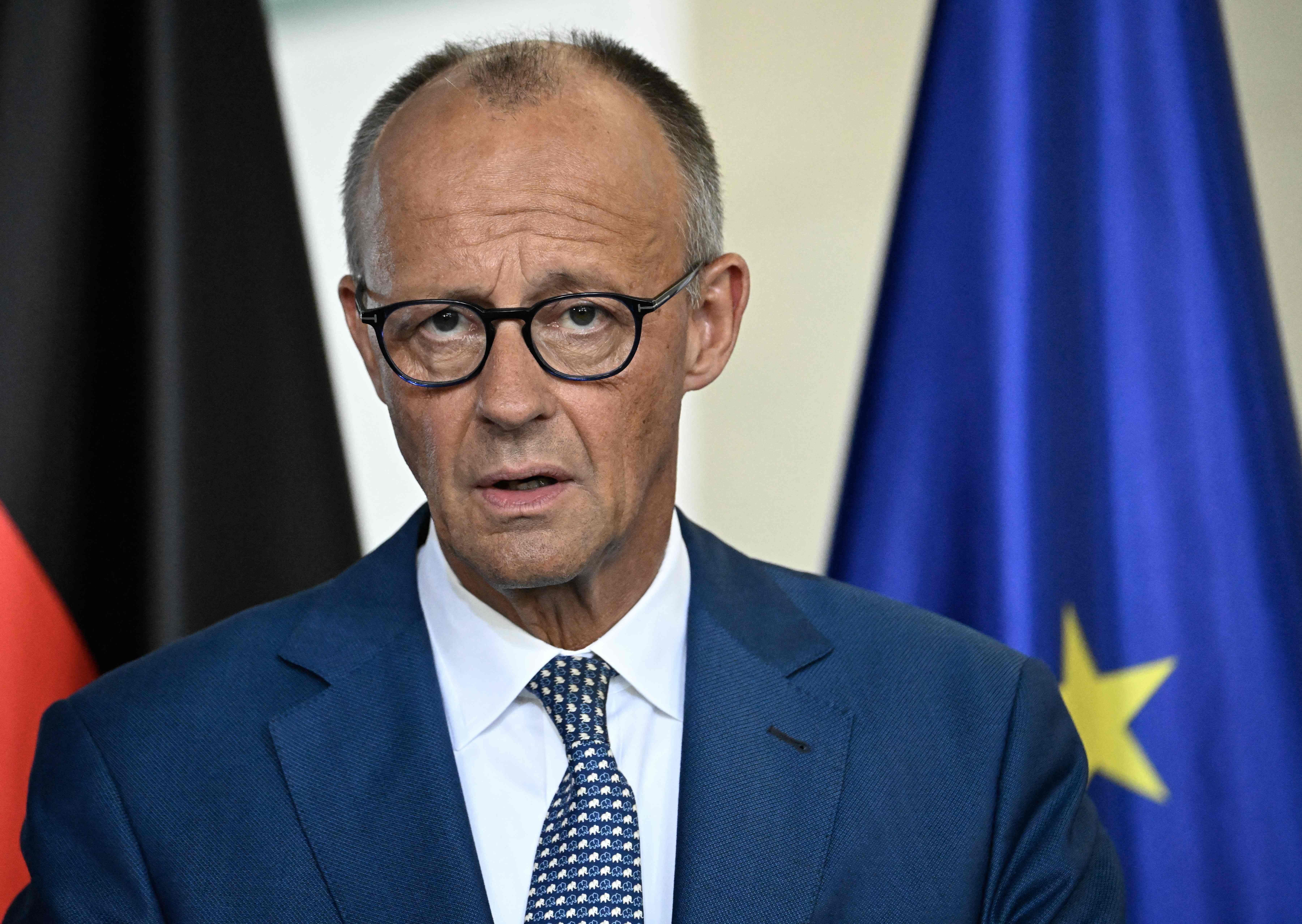 Ein Mann im Anzug spricht bei einer Pressekonferenz, hinter ihm EU- und Deutschland-Flagge.