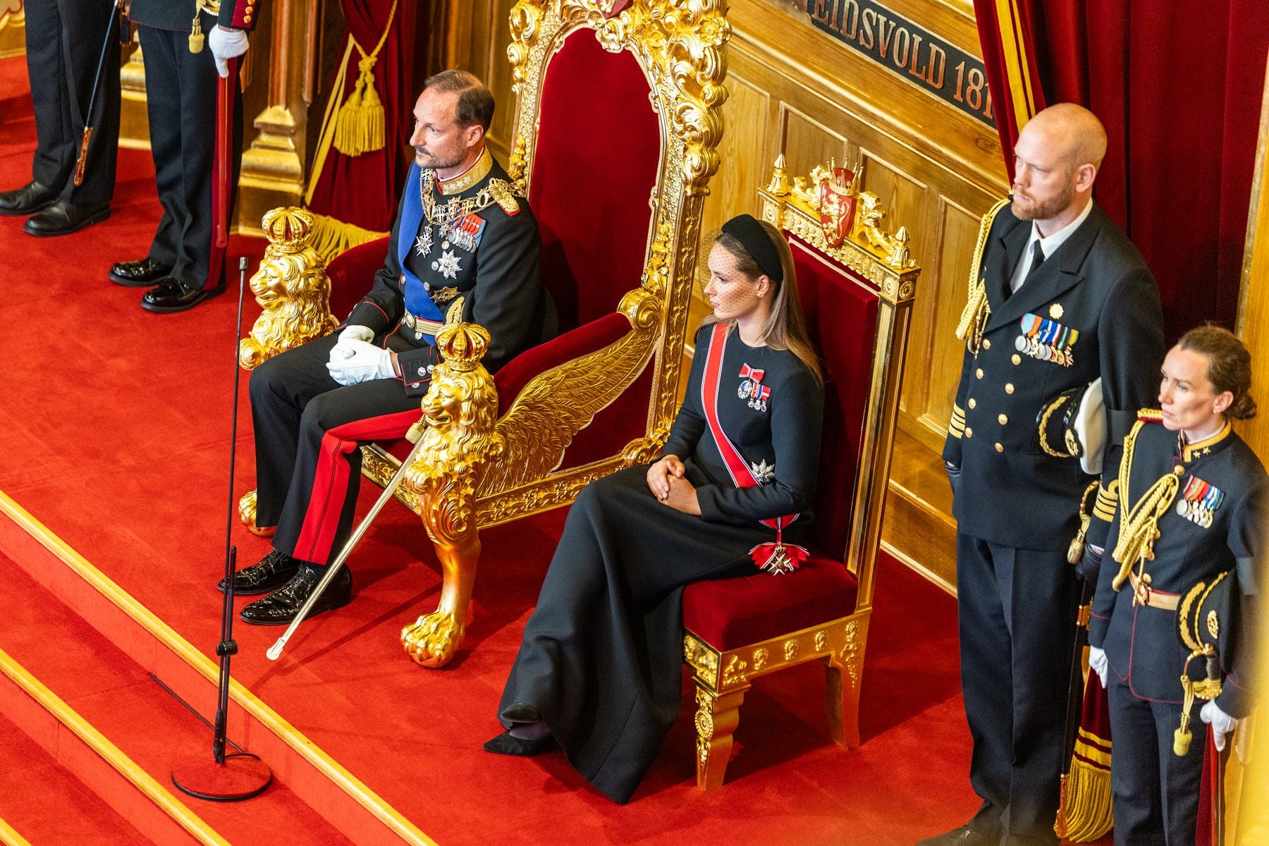 Ein Mann und eine Frau in festlicher Uniform sitzen auf goldenen Thronen im Parlamentsgebäude.