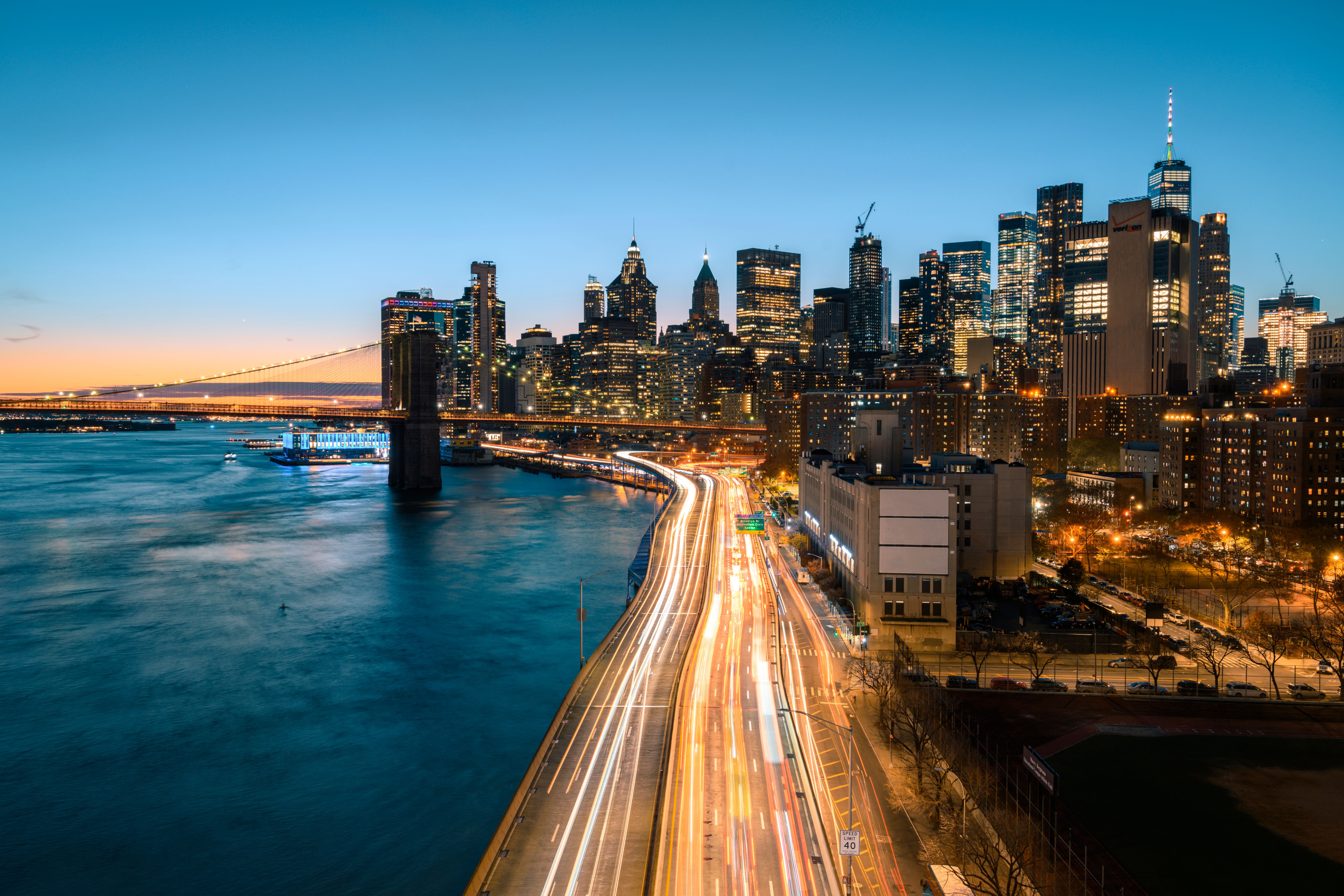 Skyline von Lower Manhattan bei Abenddämmerung mit beleuchteten Gebäuden und Brooklyn Bridge.