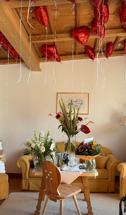 Kleiner Tisch mit Blumensträußen, gelbe Sofas und rote Herzballons an der Holzdecke.