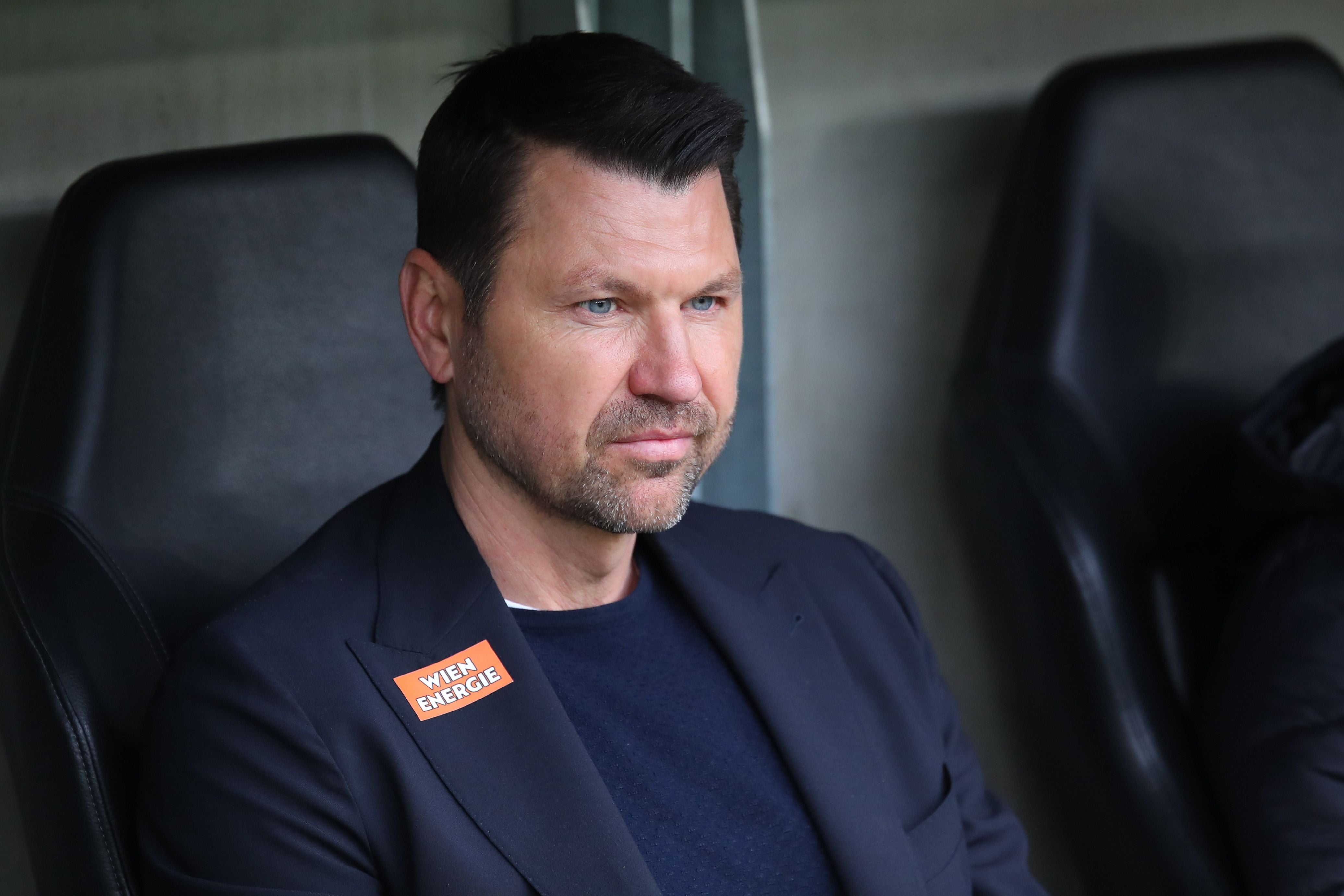 Ein Mann im dunklen Sakko sitzt nachdenklich auf einem Stadionstuhl.