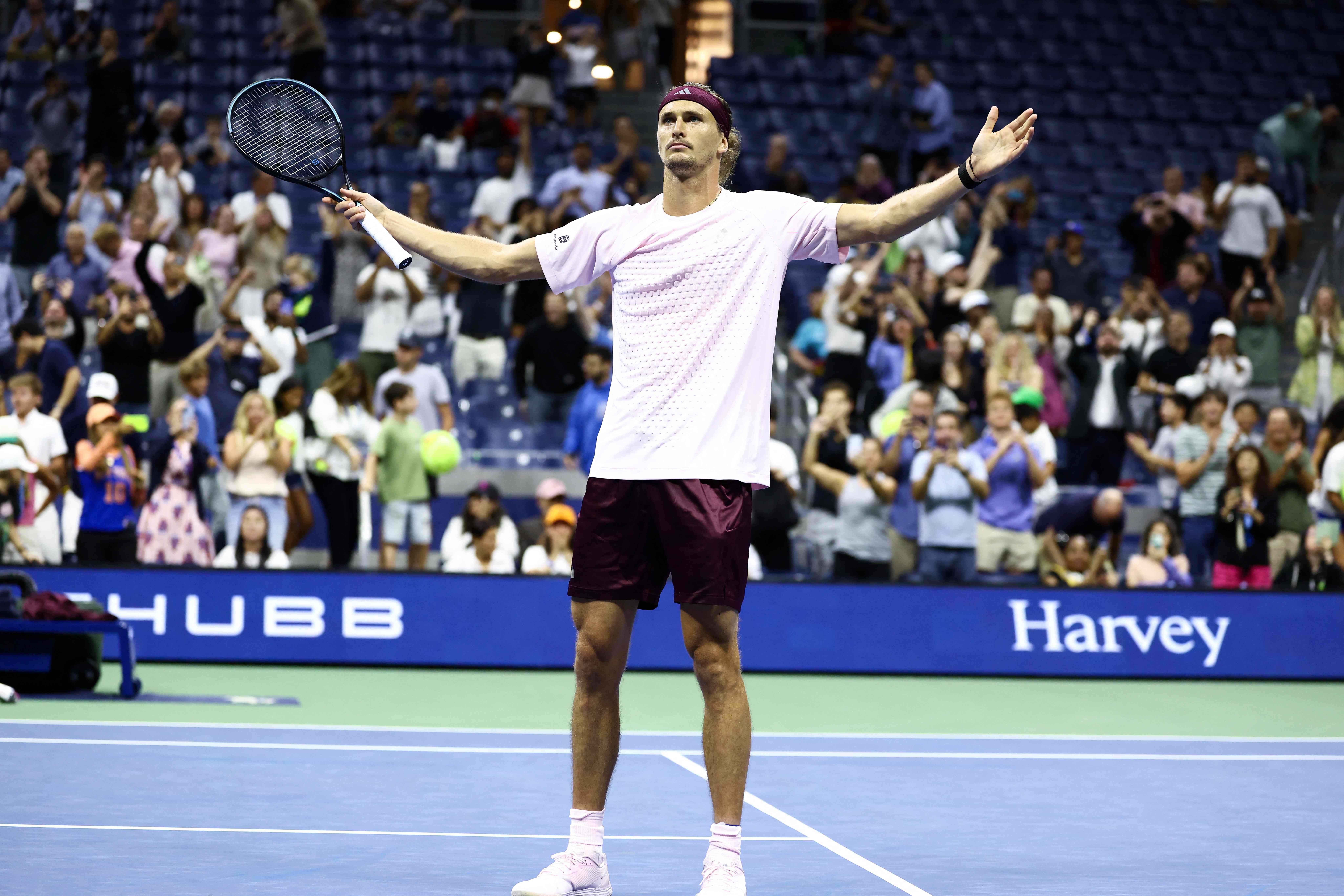 Tennisspieler jubelt mit ausgebreiteten Armen auf dem Platz, Zuschauer klatschen im Hintergrund.