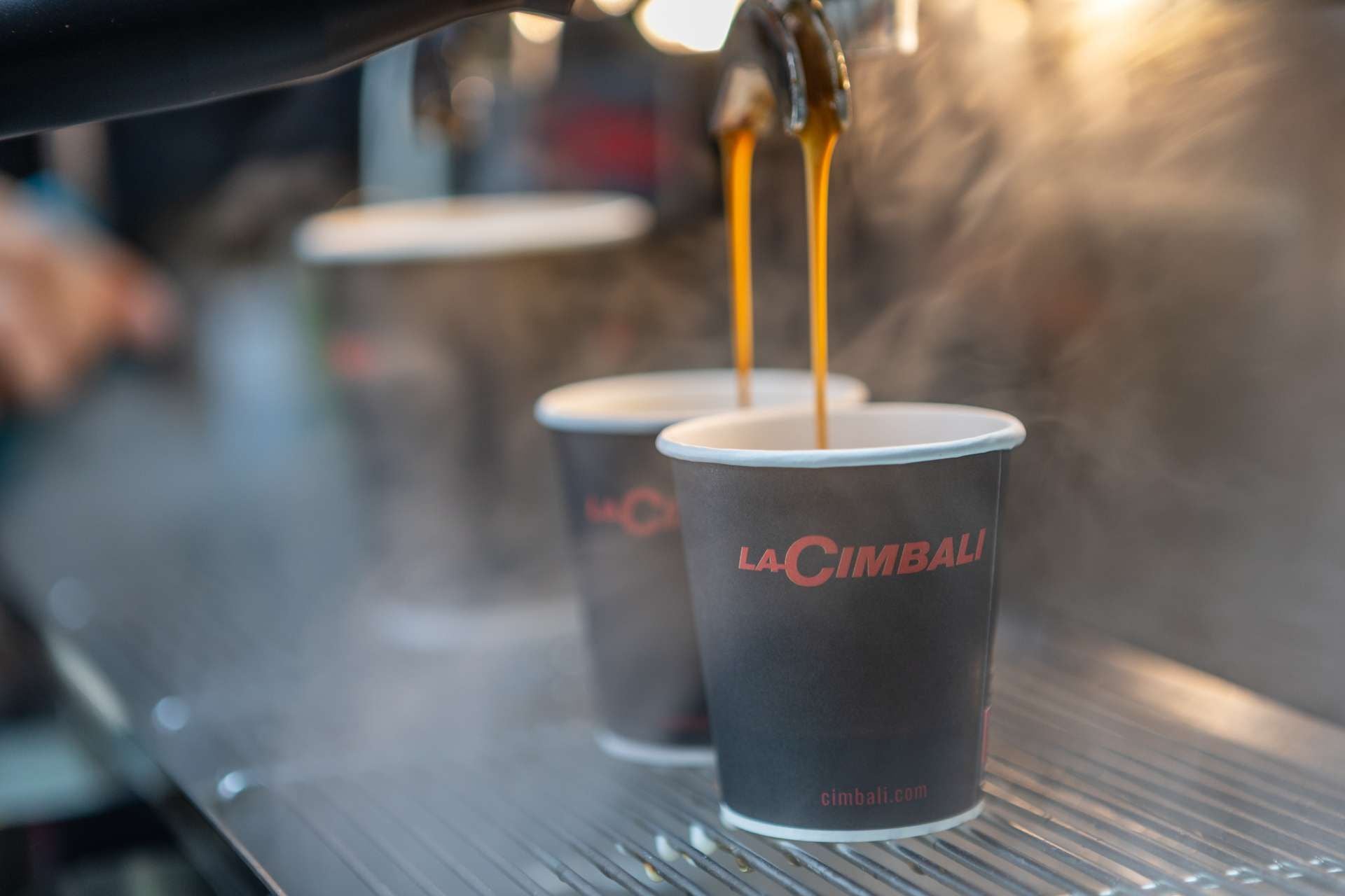 Zwei Pappbecher werden direkt aus einer Kaffeemaschine mit Kaffee befüllt.