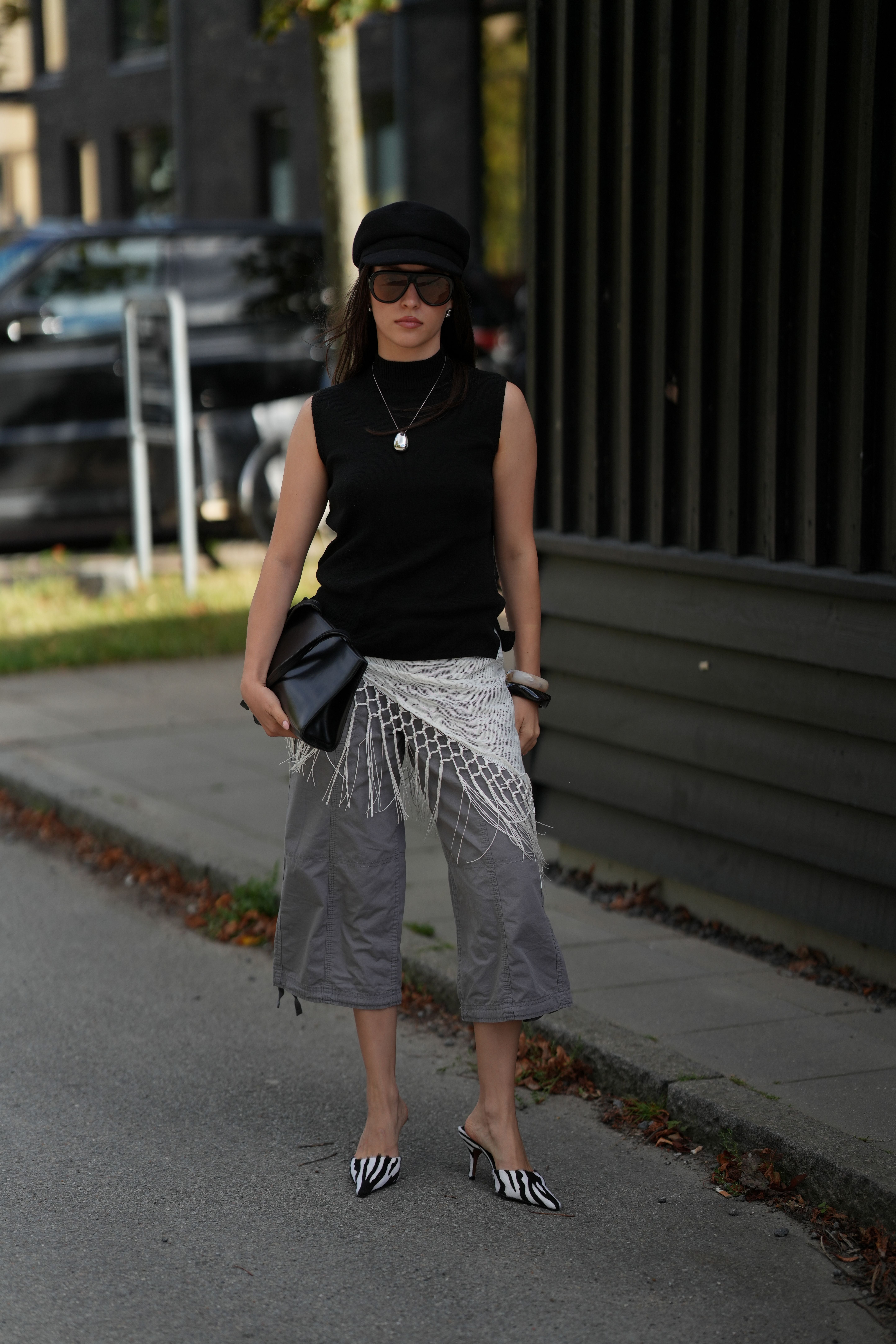 Frau mit schwarzem Top, grauer Cargo-Hose, Fransenrock, Zebra-Absätzen und schwarzer Mütze.