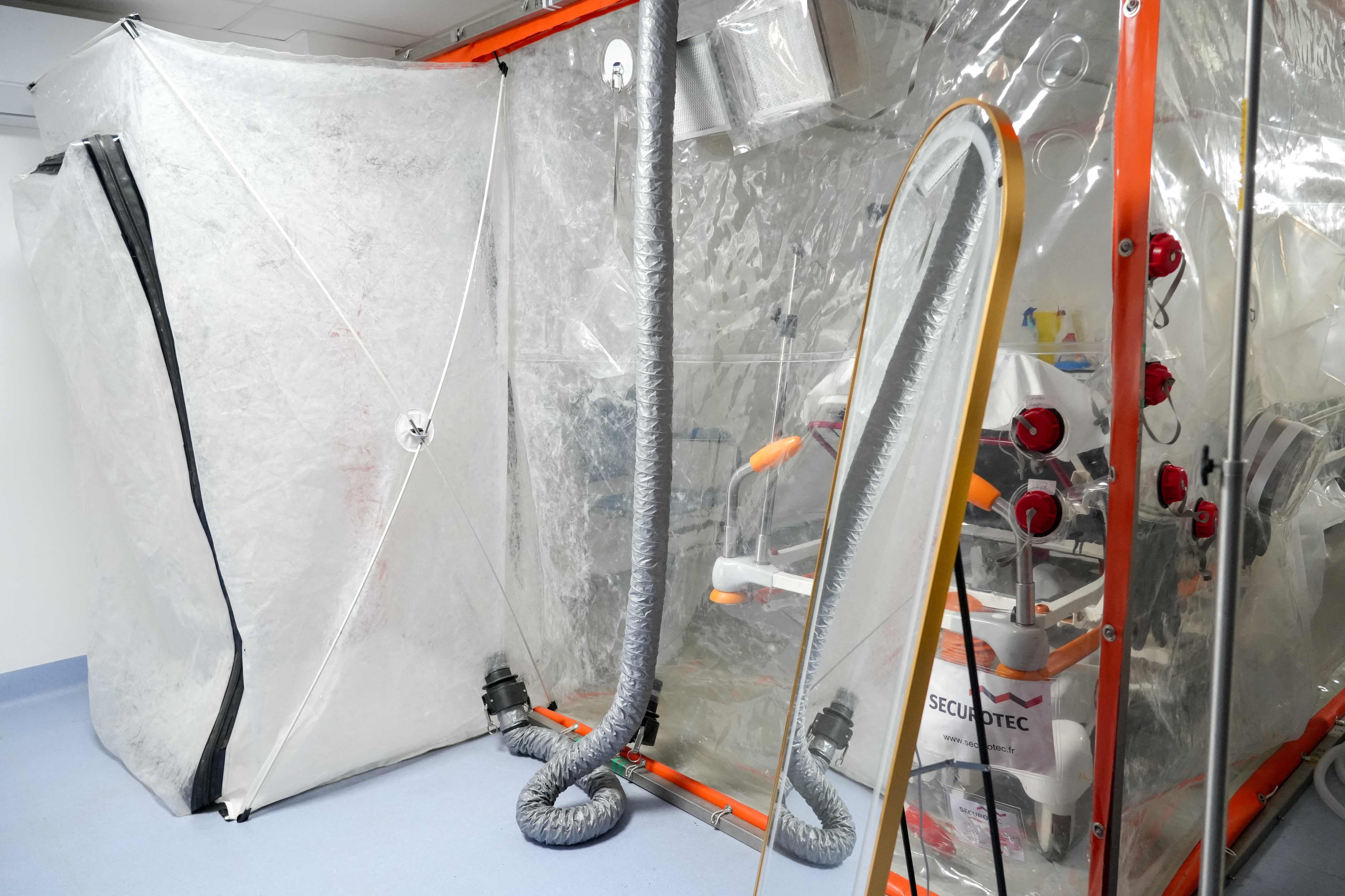 Isolierstation mit durchsichtigen Plastikwänden und Schläuchen in einem Krankenhausraum.