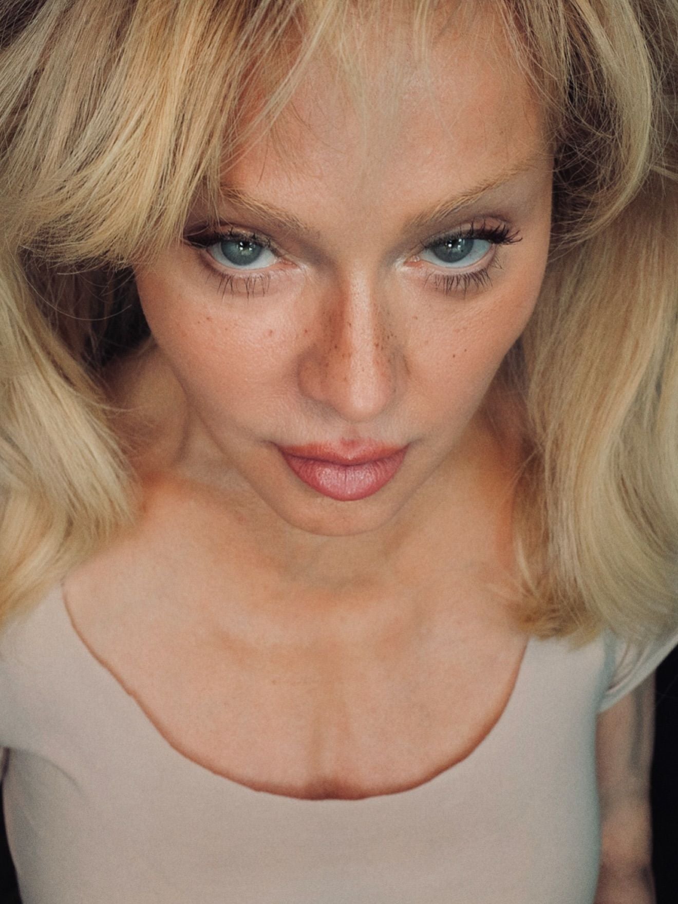 Nahaufnahme einer Frau mit blonden Haaren und blaugrünen Augen, die nach unten blickt.