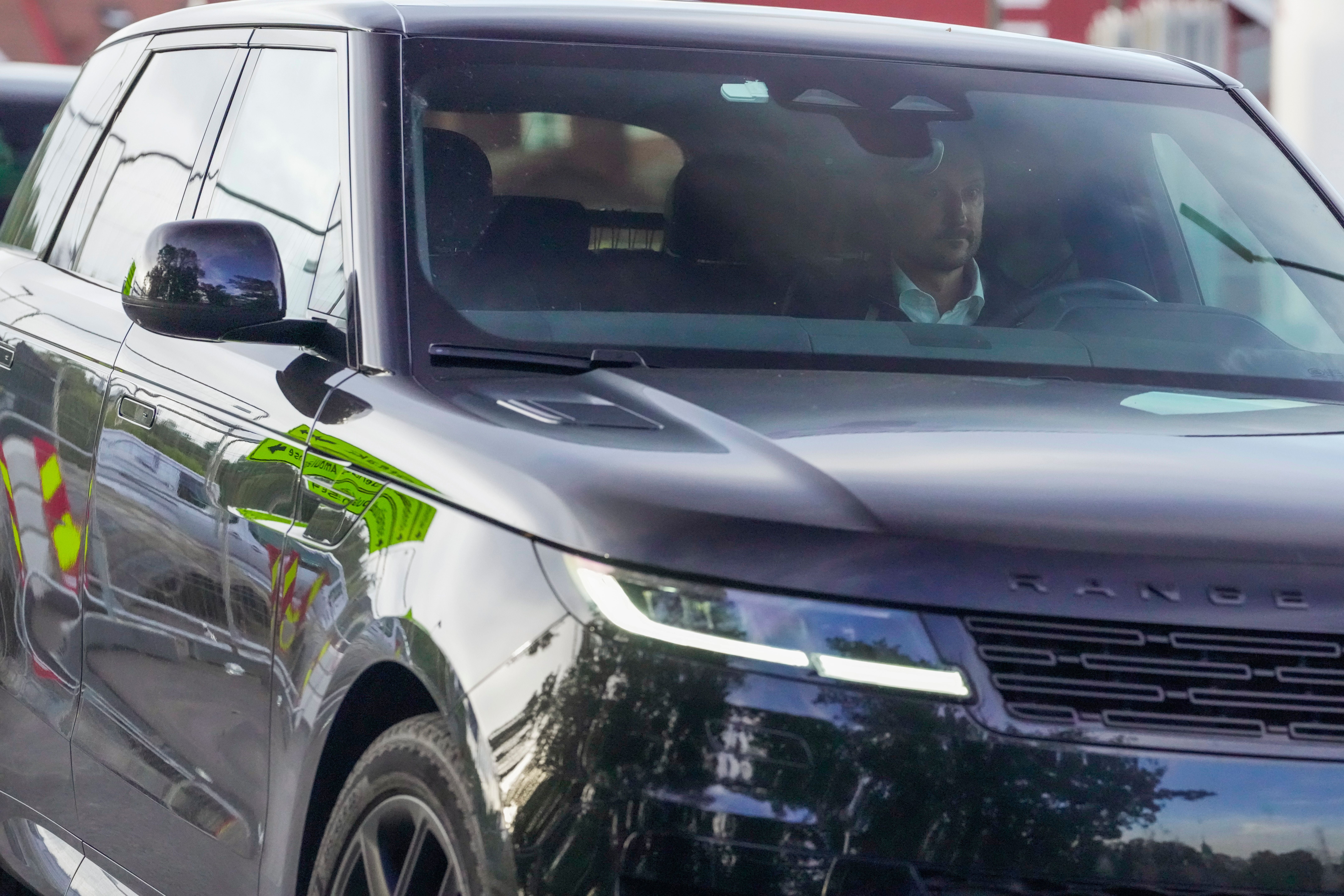 Ein Mann fährt einen schwarzen Range Rover mit reflektierenden gelben Warnwesten im Hintergrund.
